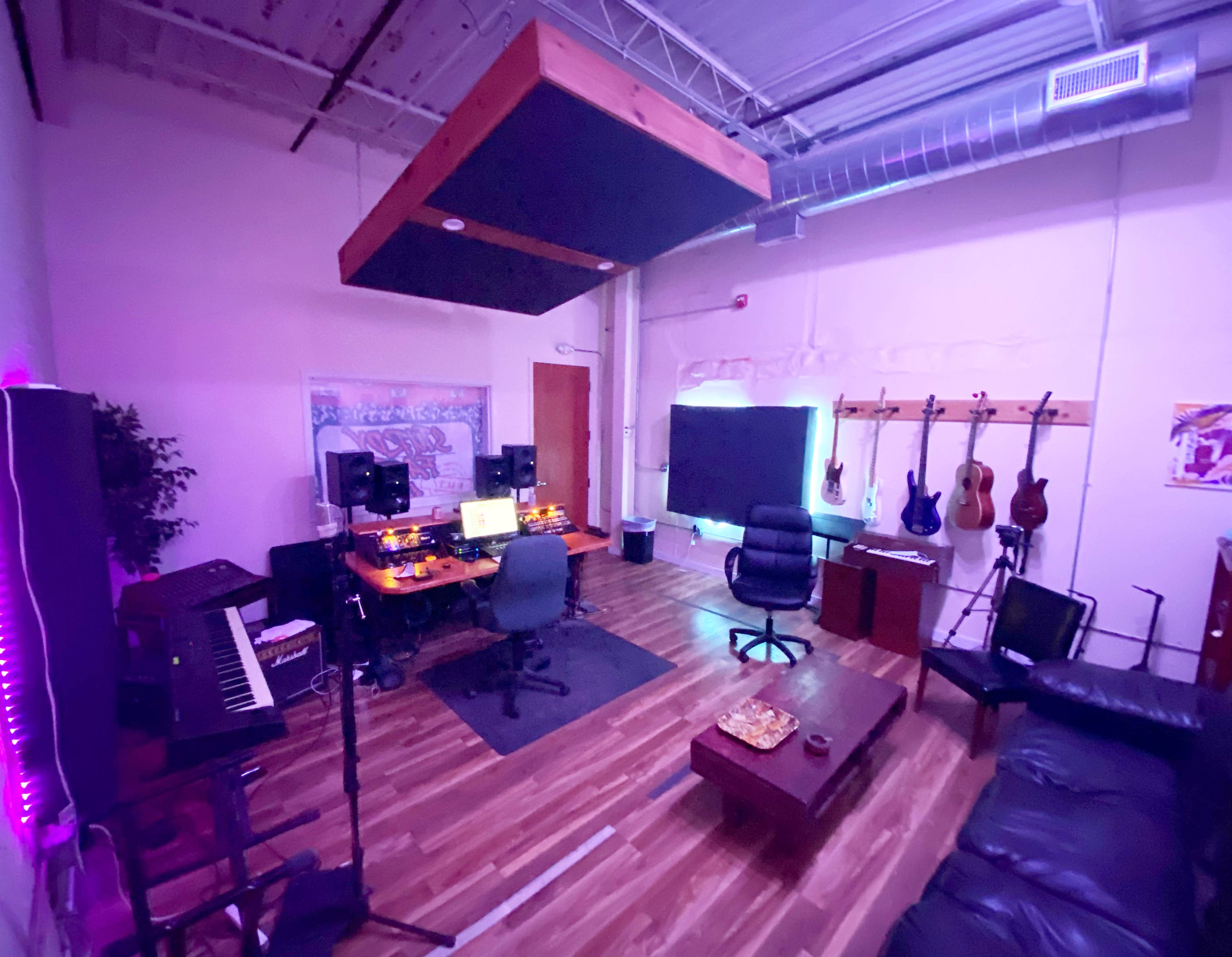 A music studio equipped with a desktop setup, various musical instruments on the walls, and a seating area.