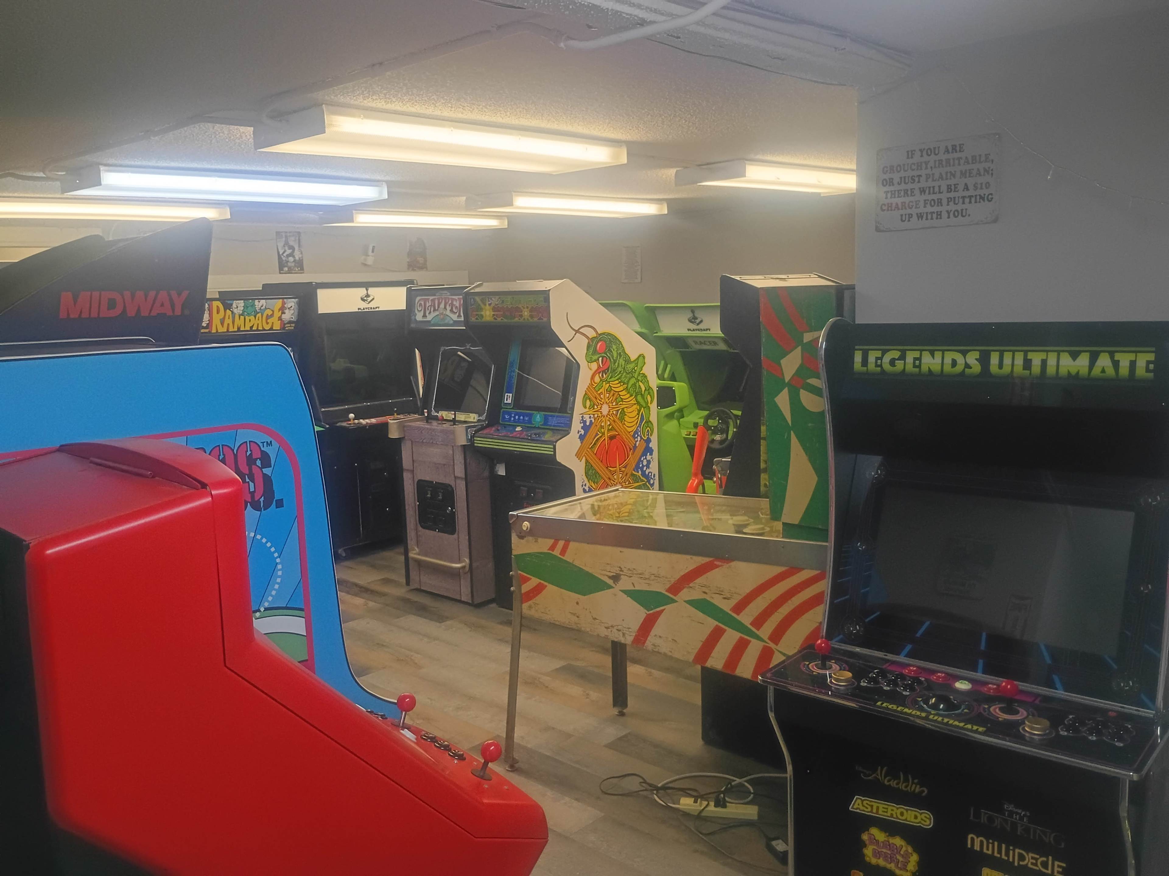 The scene shows a row of vintage arcade machines in a dimly lit room, including colorful cabinets and a pinball table.