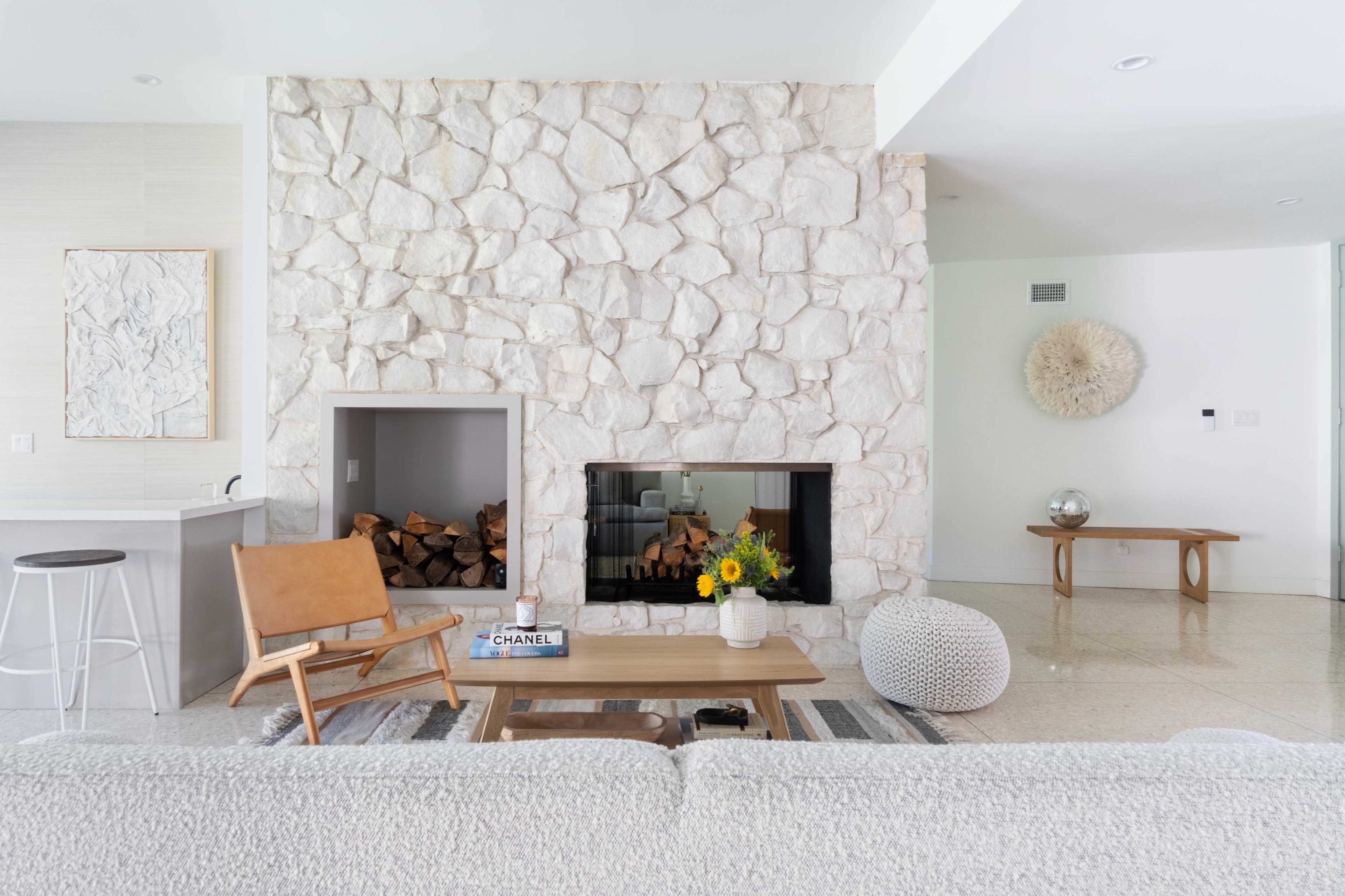 The image shows a modern living room featuring a stone fireplace, a wooden coffee table, a light gray sofa, and a minimalist decor style.