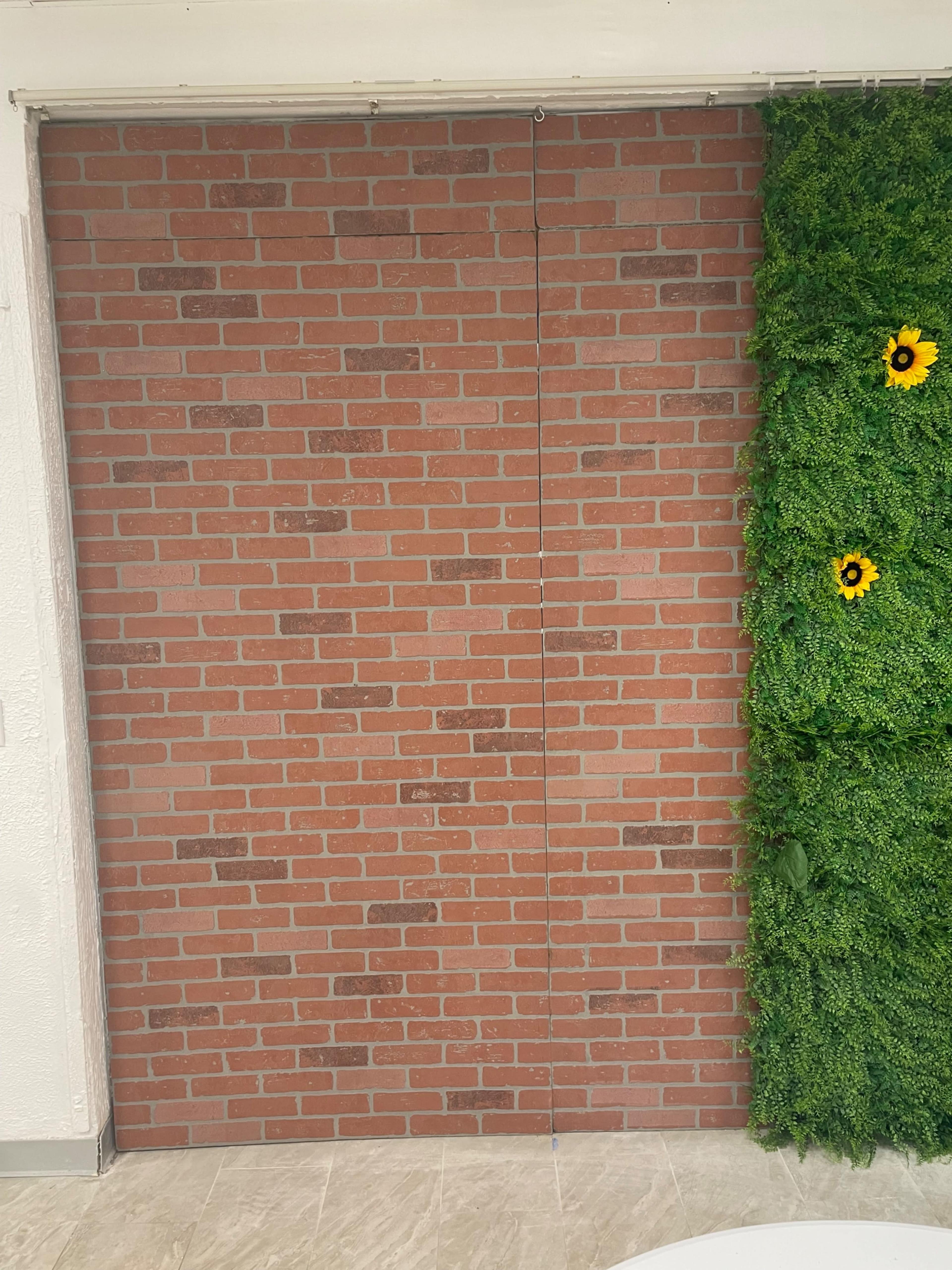 A brick wall on one side and a vertical garden with green foliage and yellow sunflowers on the other side.
