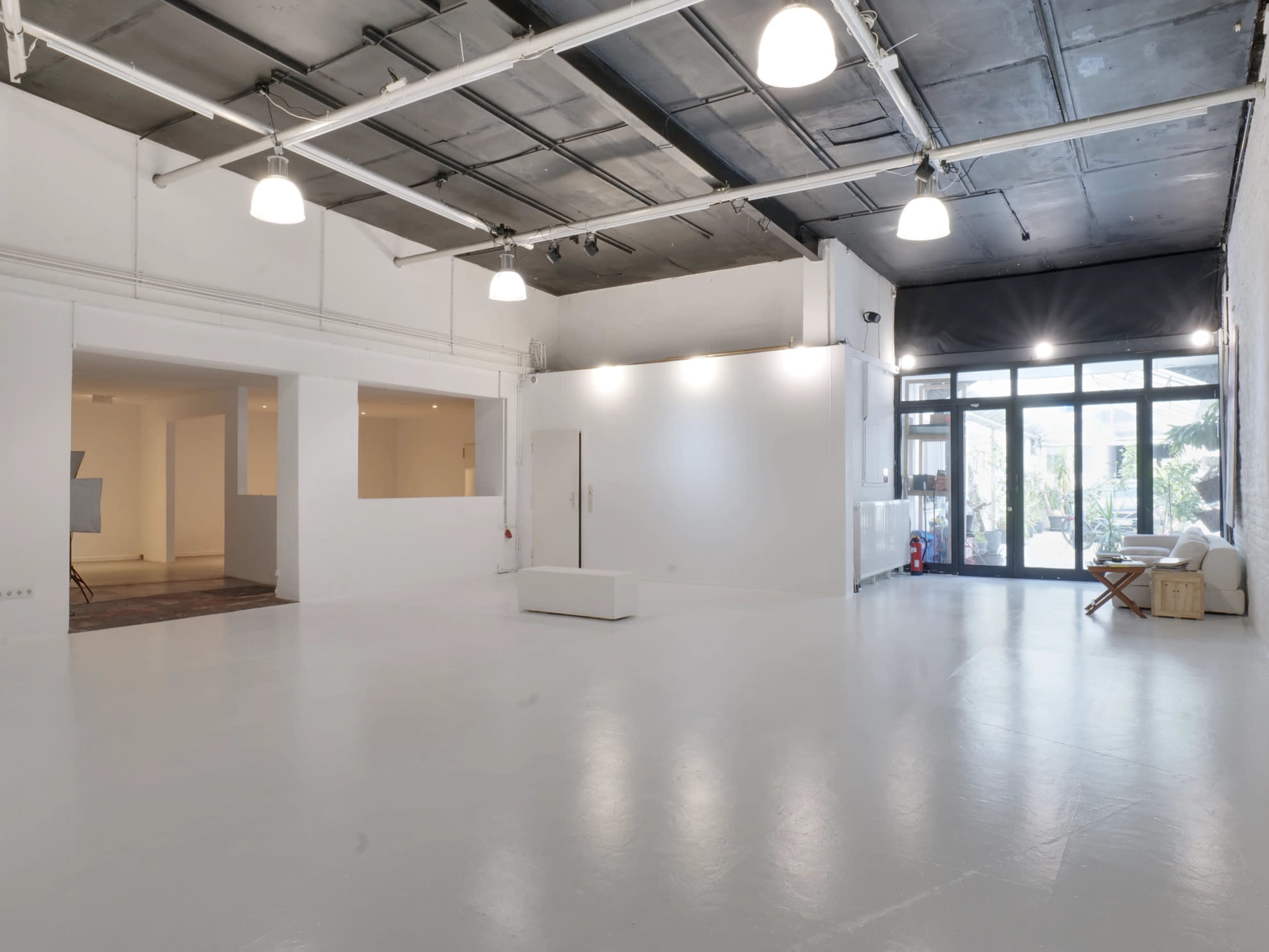 The image shows a spacious, empty modern studio with white walls, polished floors, and large windows.