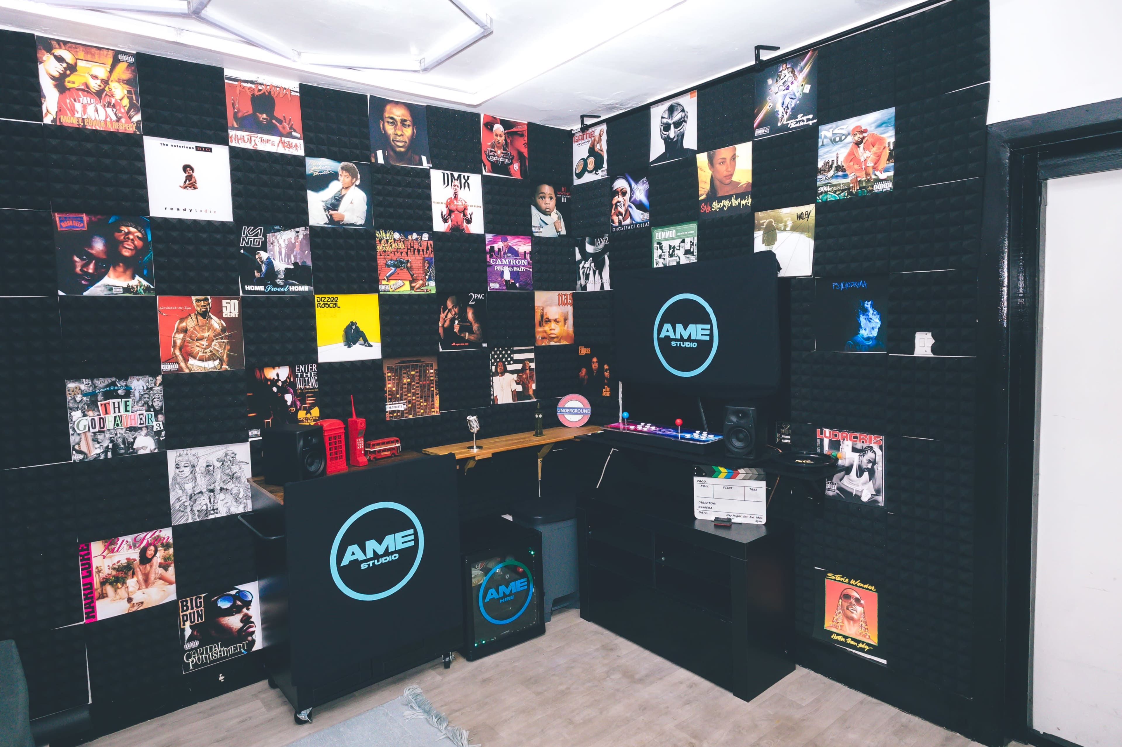 The image shows a music studio with a wall covered in posters of various hip-hop artists, featuring a DJ setup and equipment along one side.