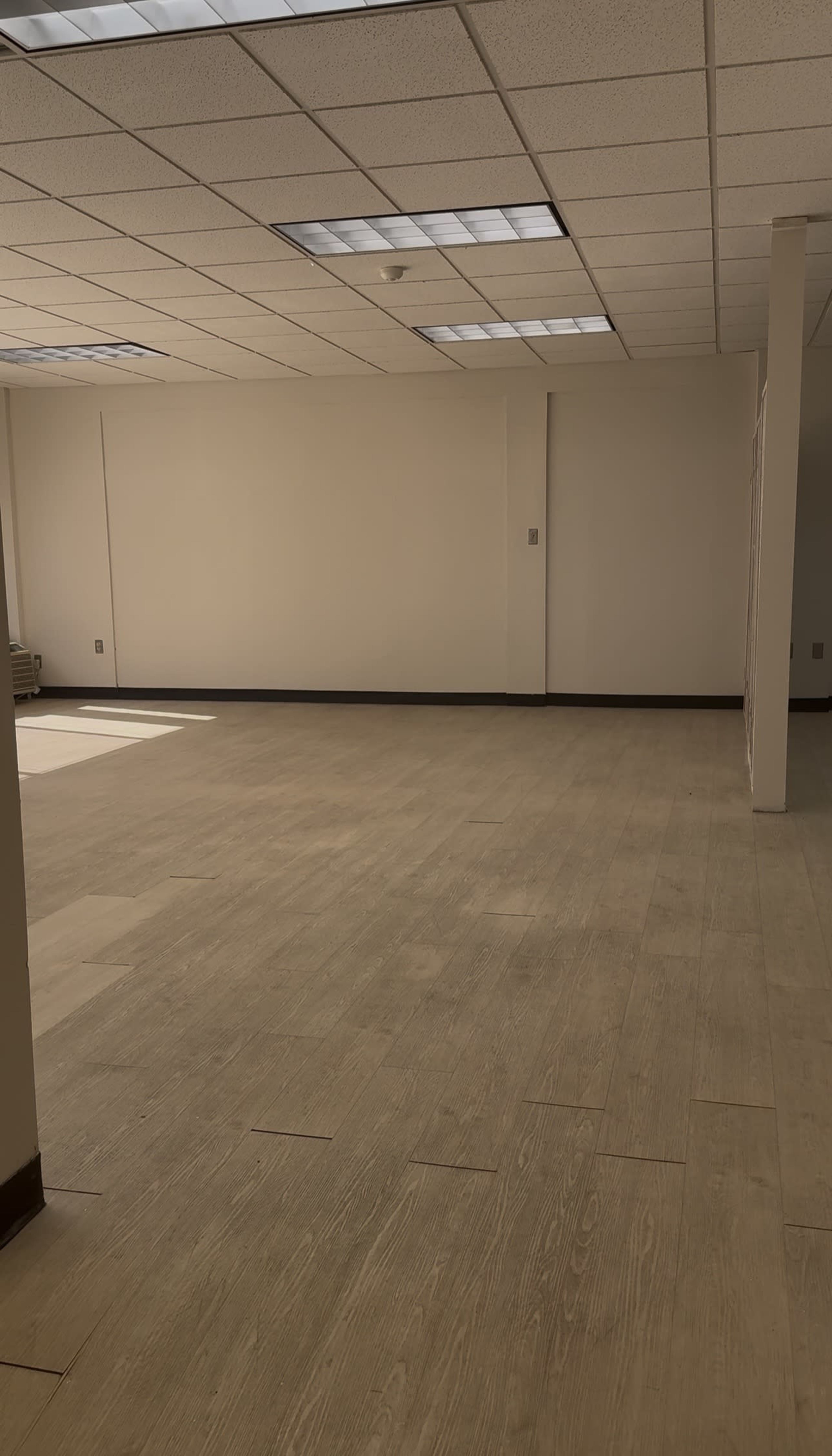 The image shows an empty, well-lit room with light-colored wooden flooring and white walls.