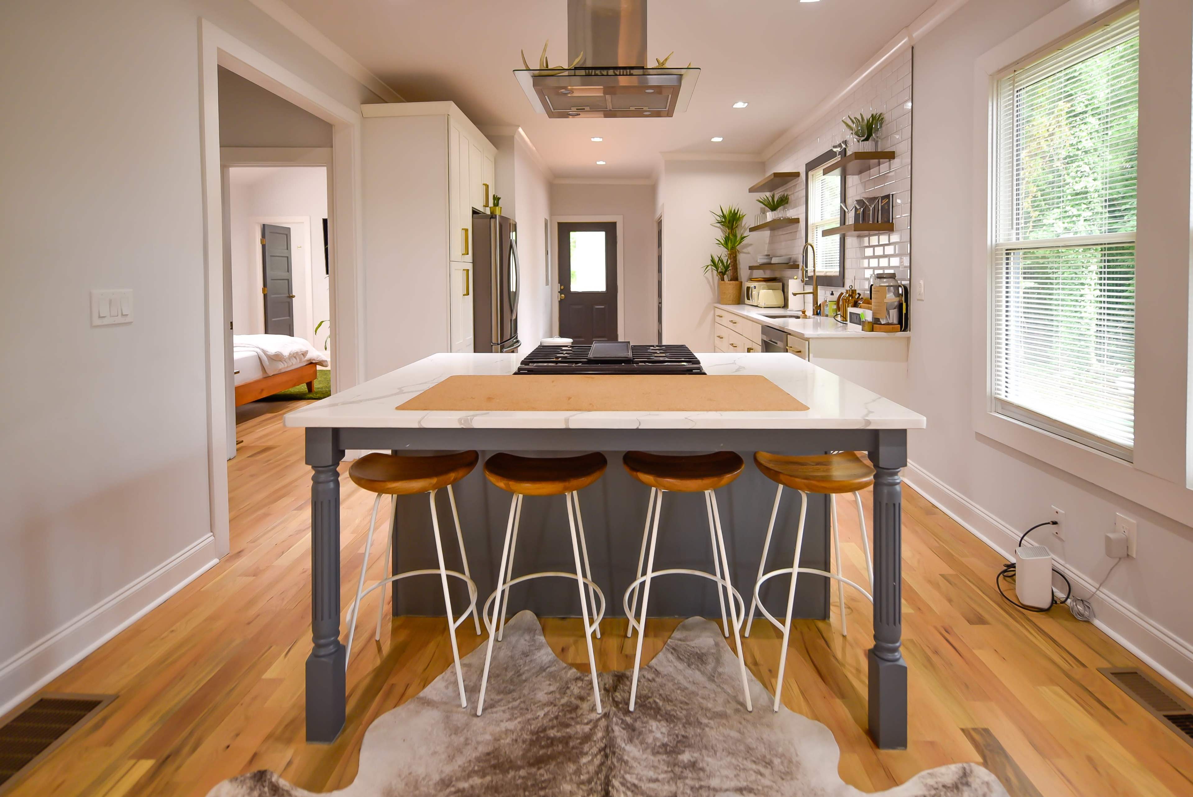 A modern kitchen features a central island with three bar stools, surrounded by white cabinetry and wooden flooring.