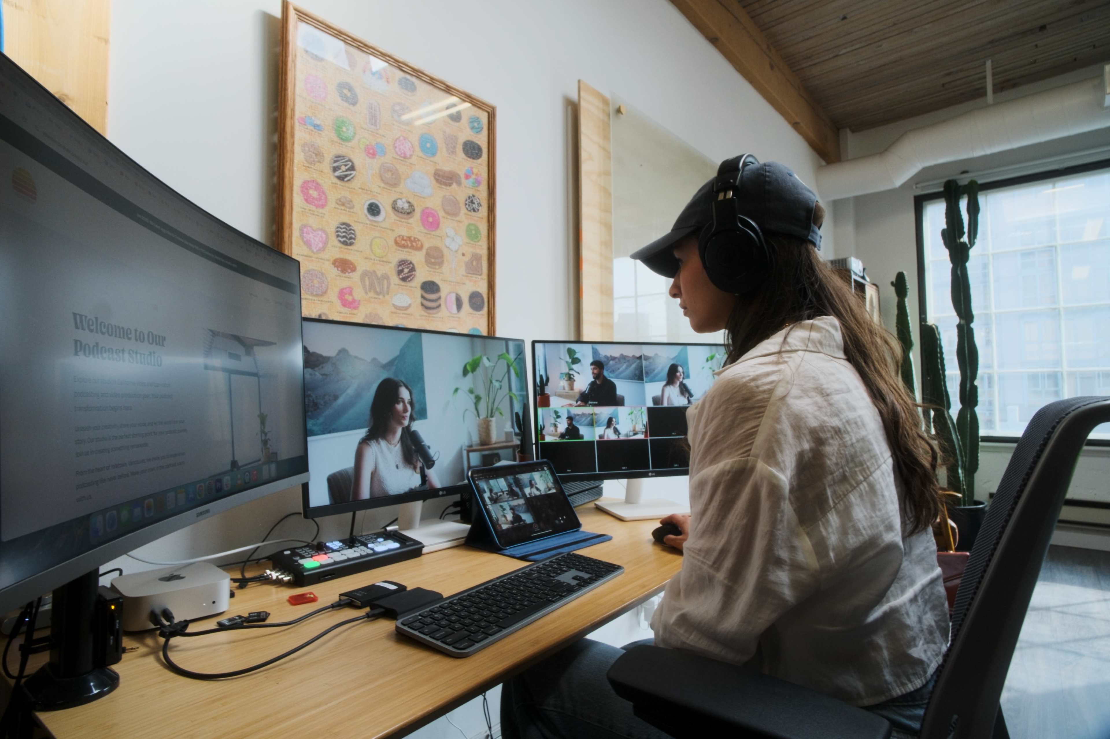 A person with headphones sits at a desk, engaging in a video conference with multiple screens displaying different participants.
