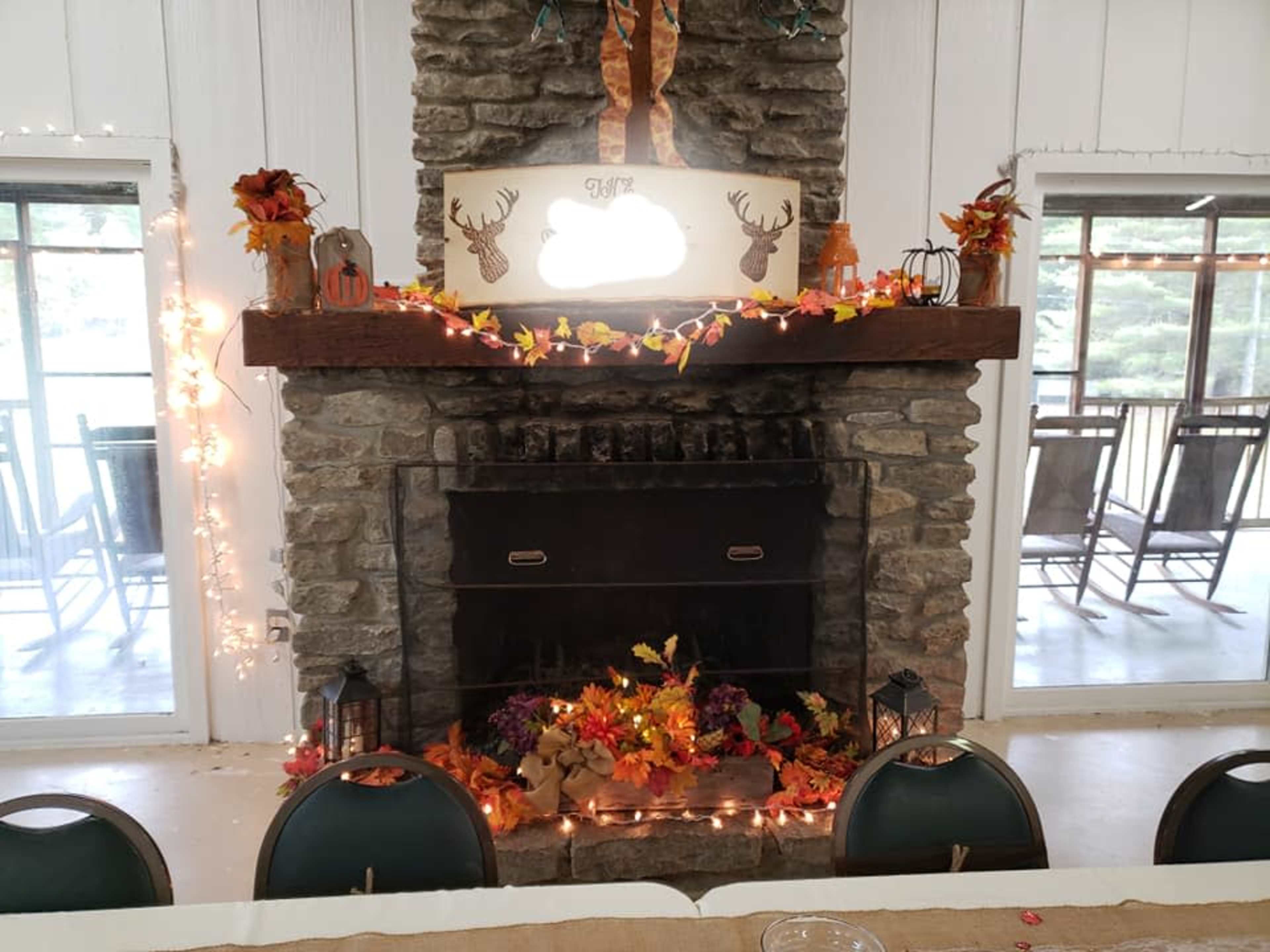 A stone fireplace adorned with autumn decorations, surrounded by windows overlooking a deck.