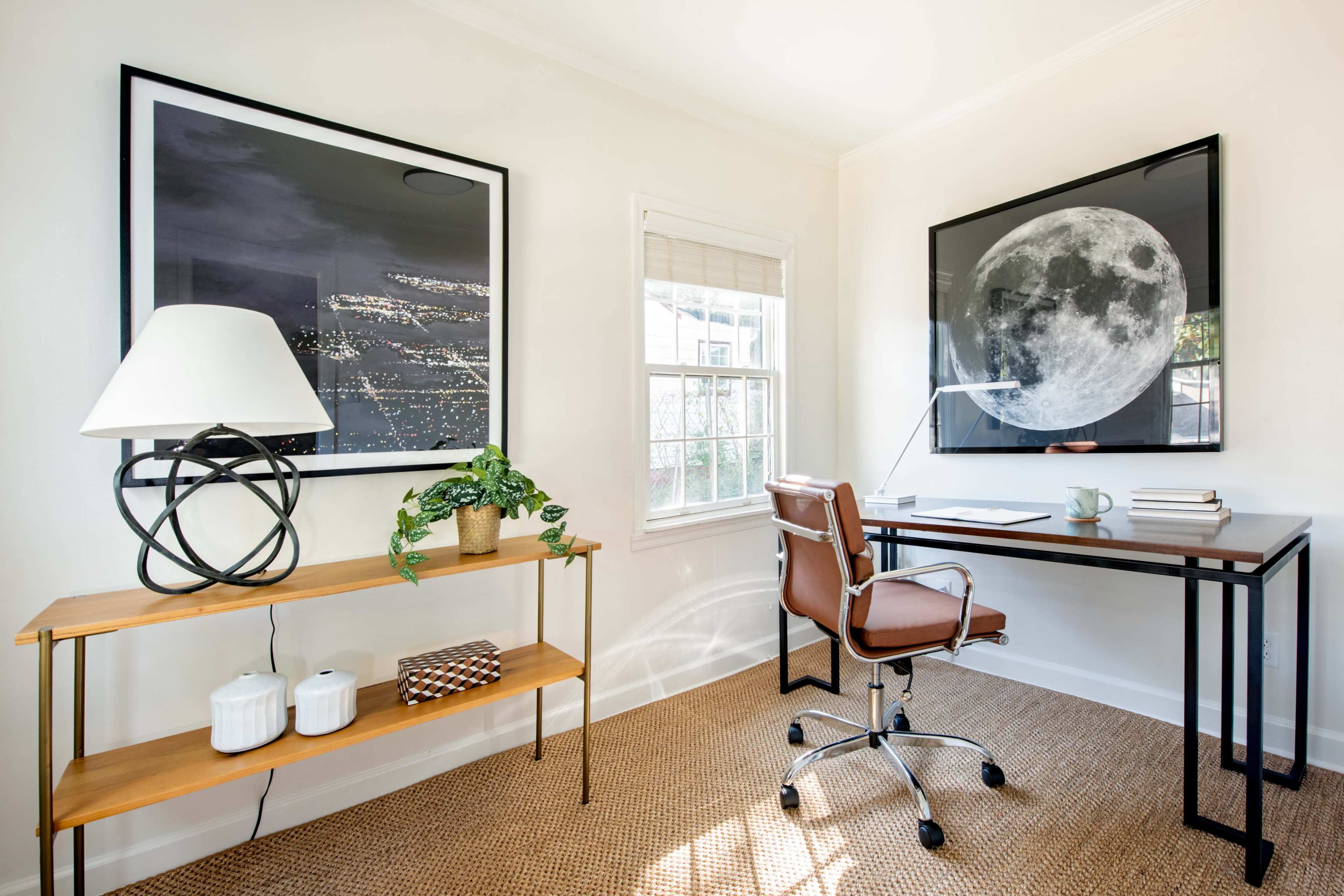 A modern office space with a desk, a rolling chair, and two large framed prints of the night sky and the moon on the walls.