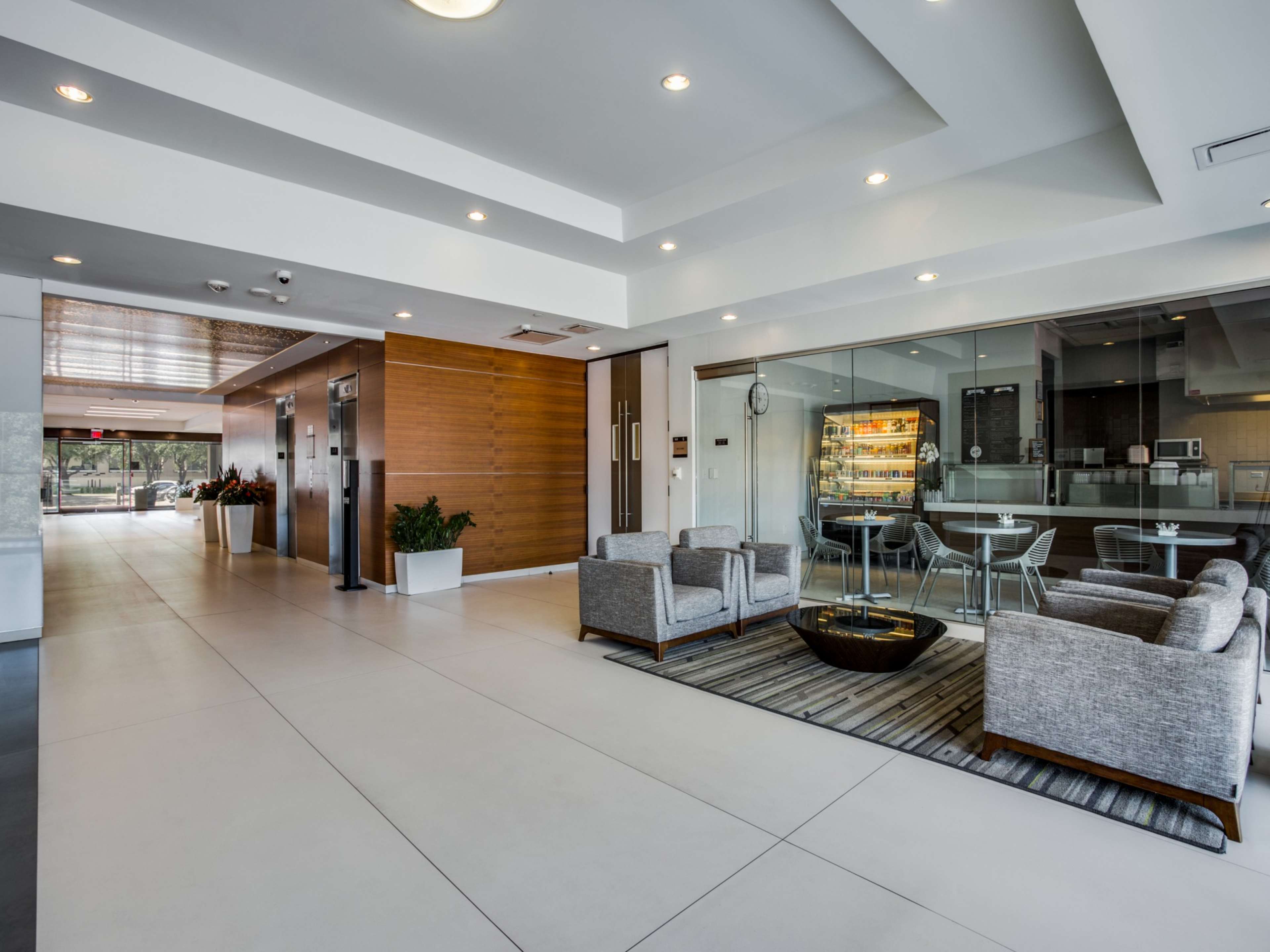 The image shows a modern lobby area with a reception desk, comfortable seating, and a glass-walled meeting room.