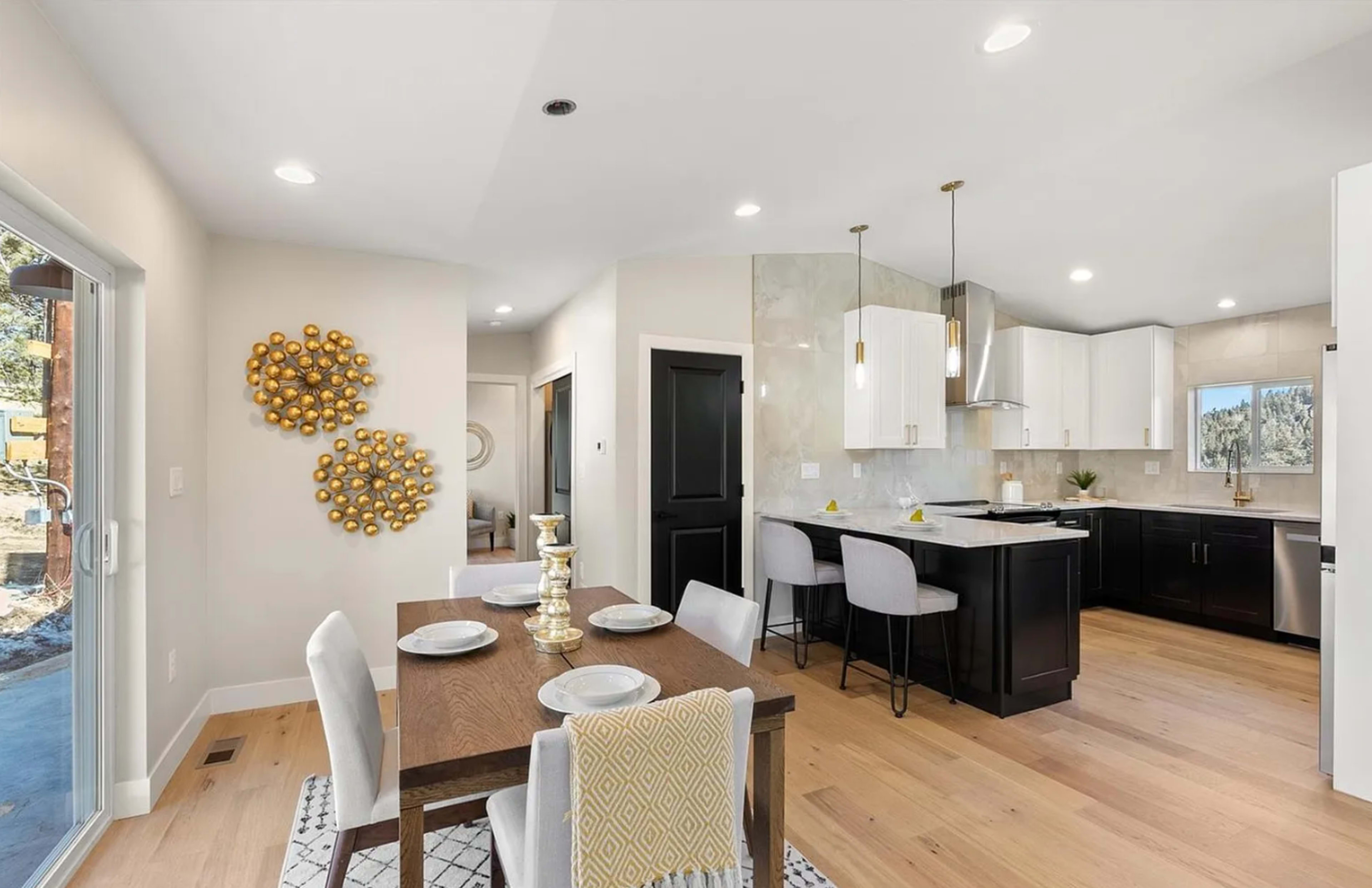 The image shows a modern kitchen and dining area featuring a wooden table with silver accents, gray bar stools, and bright white cabinets.