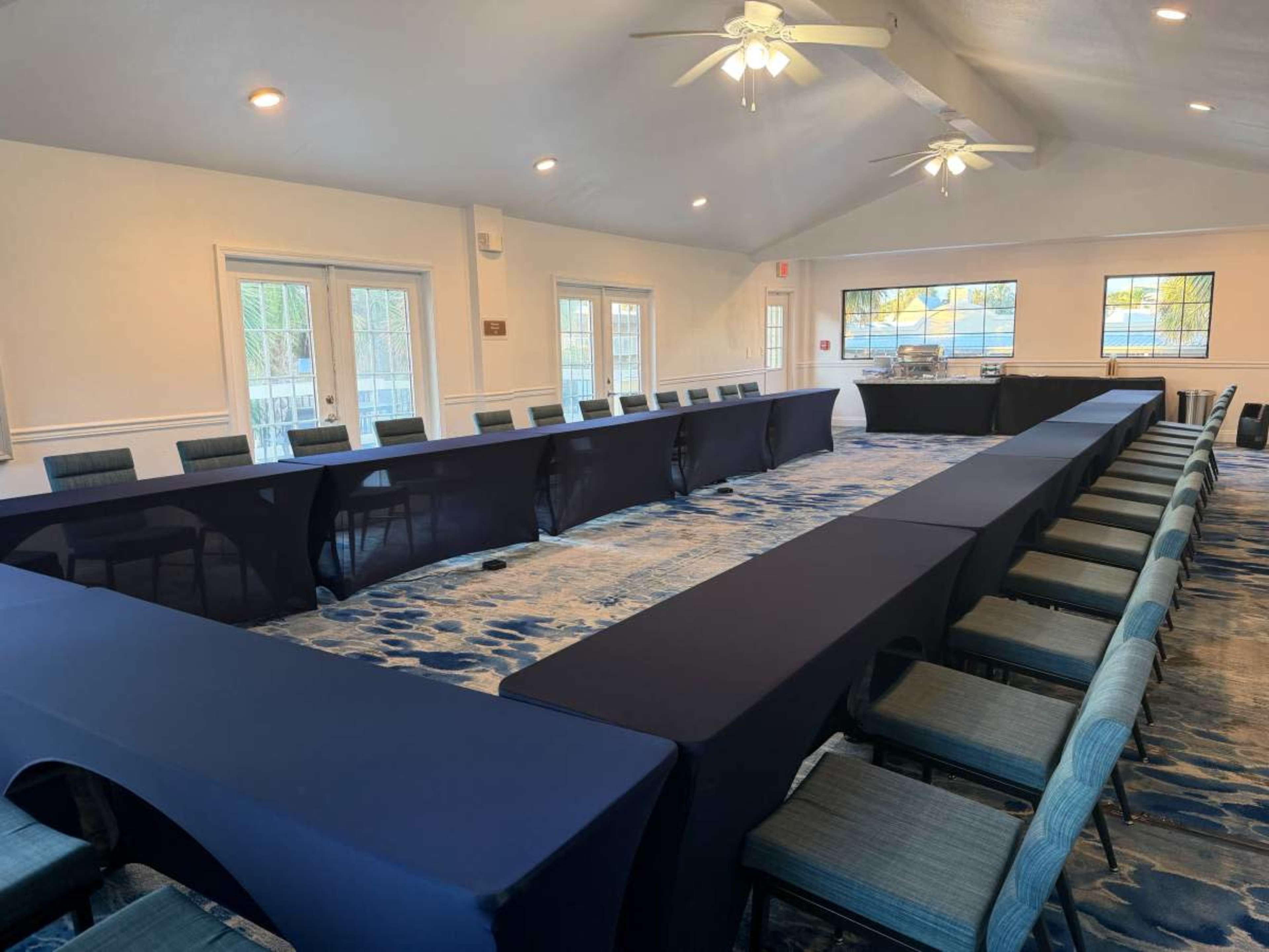 A large meeting room is set up with a U-shaped arrangement of tables covered in dark blue linens, surrounded by chairs in a modern design.