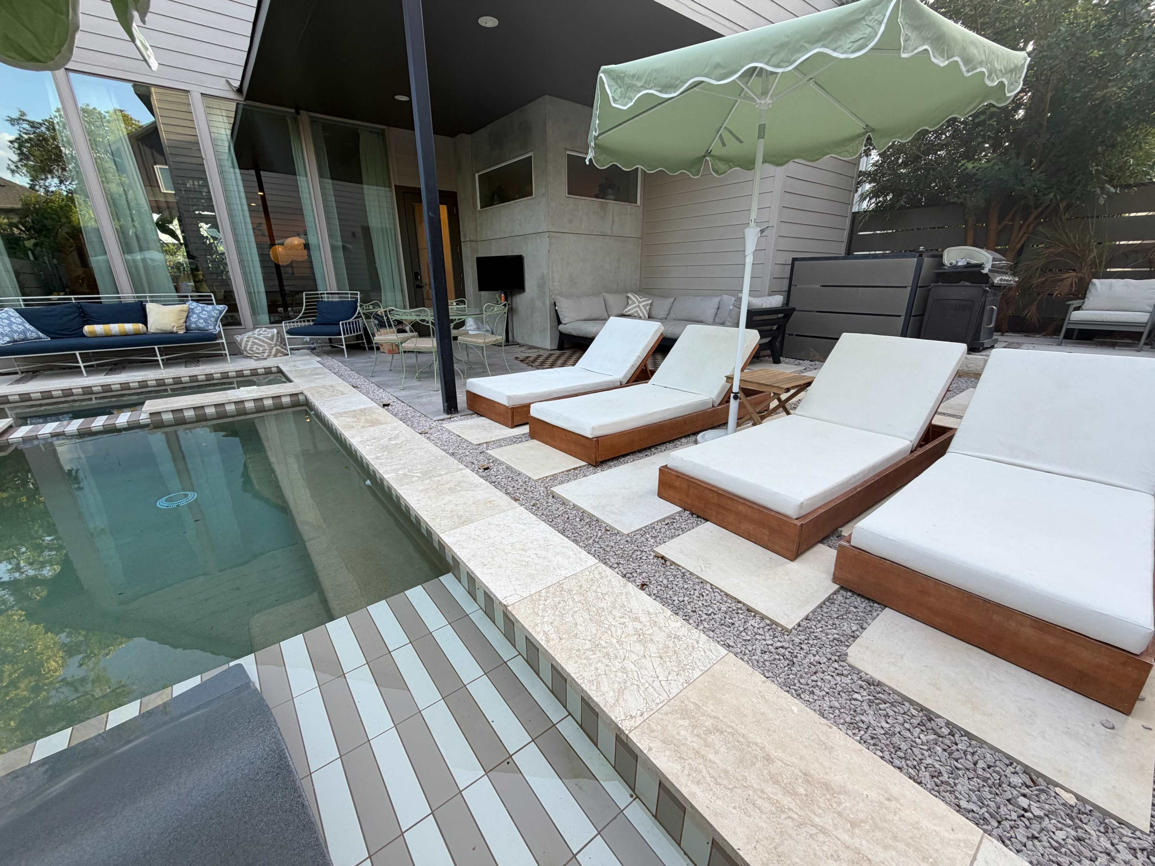 The image shows a modern outdoor pool area with three lounge chairs beside a pool, surrounded by a stone and gravel patio.