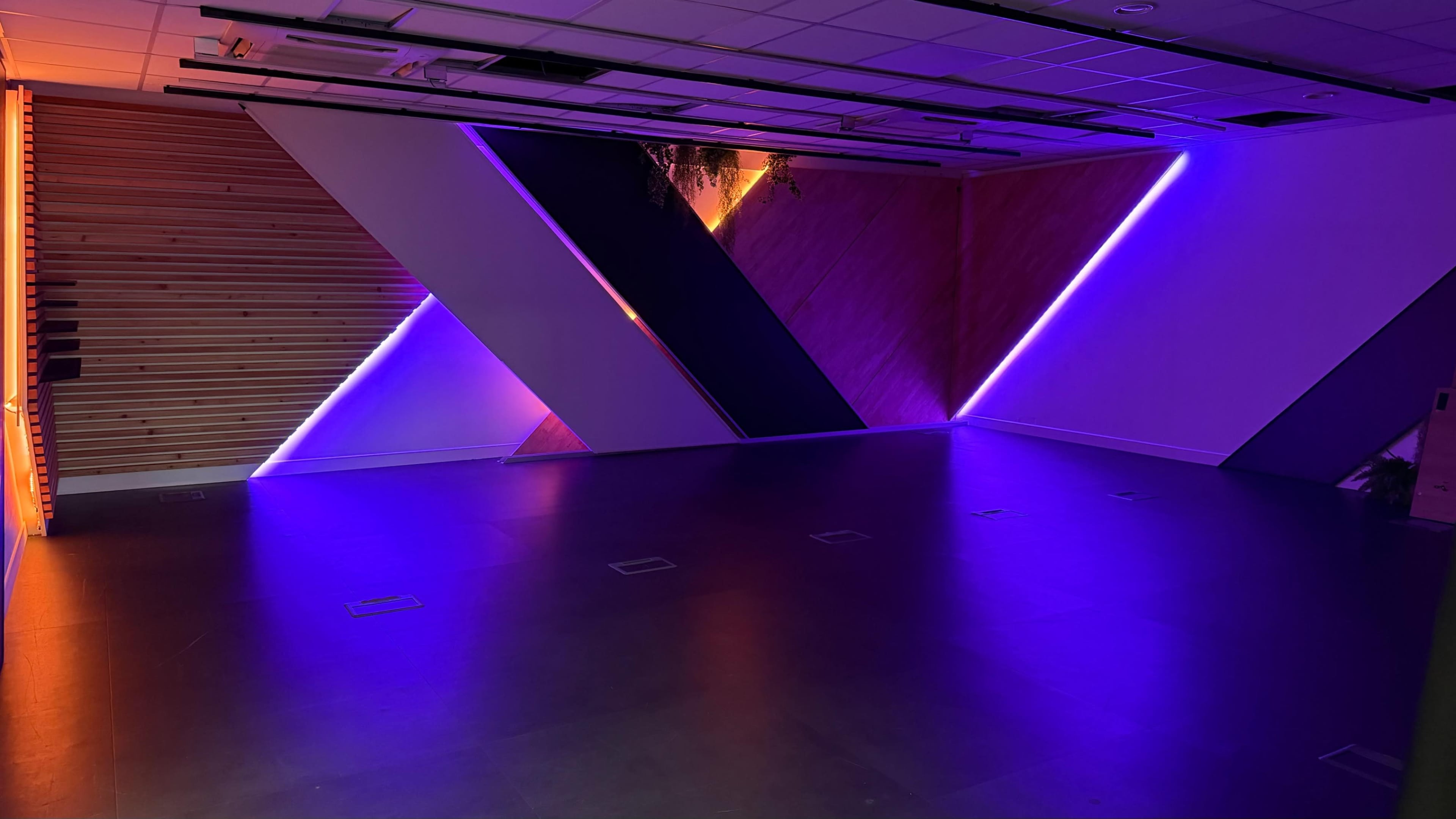 The image shows a modern interior space with geometric wall designs illuminated by purple lighting.