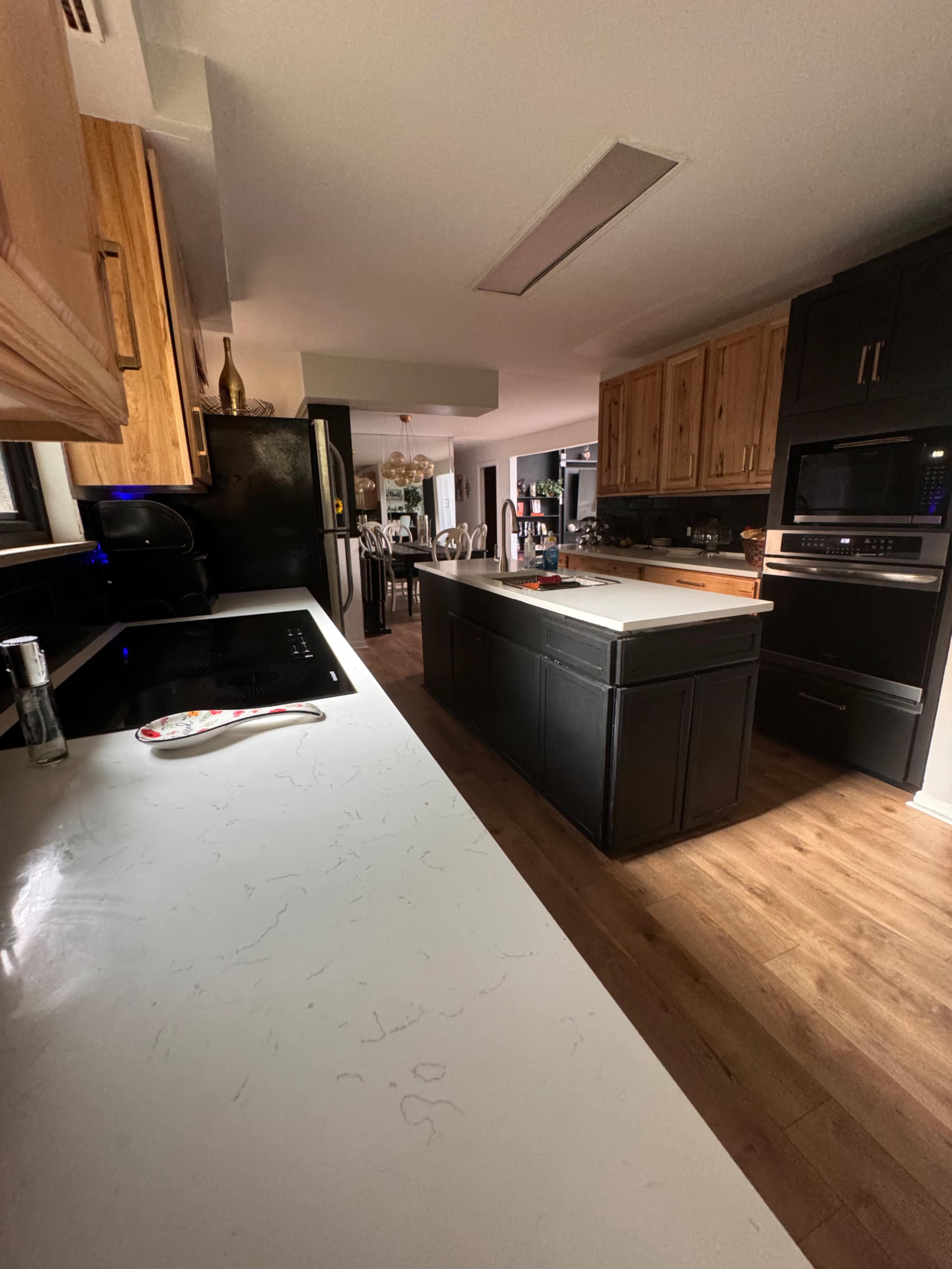 The image shows a modern kitchen with a combination of dark cabinetry and light countertops, featuring an island in the center.