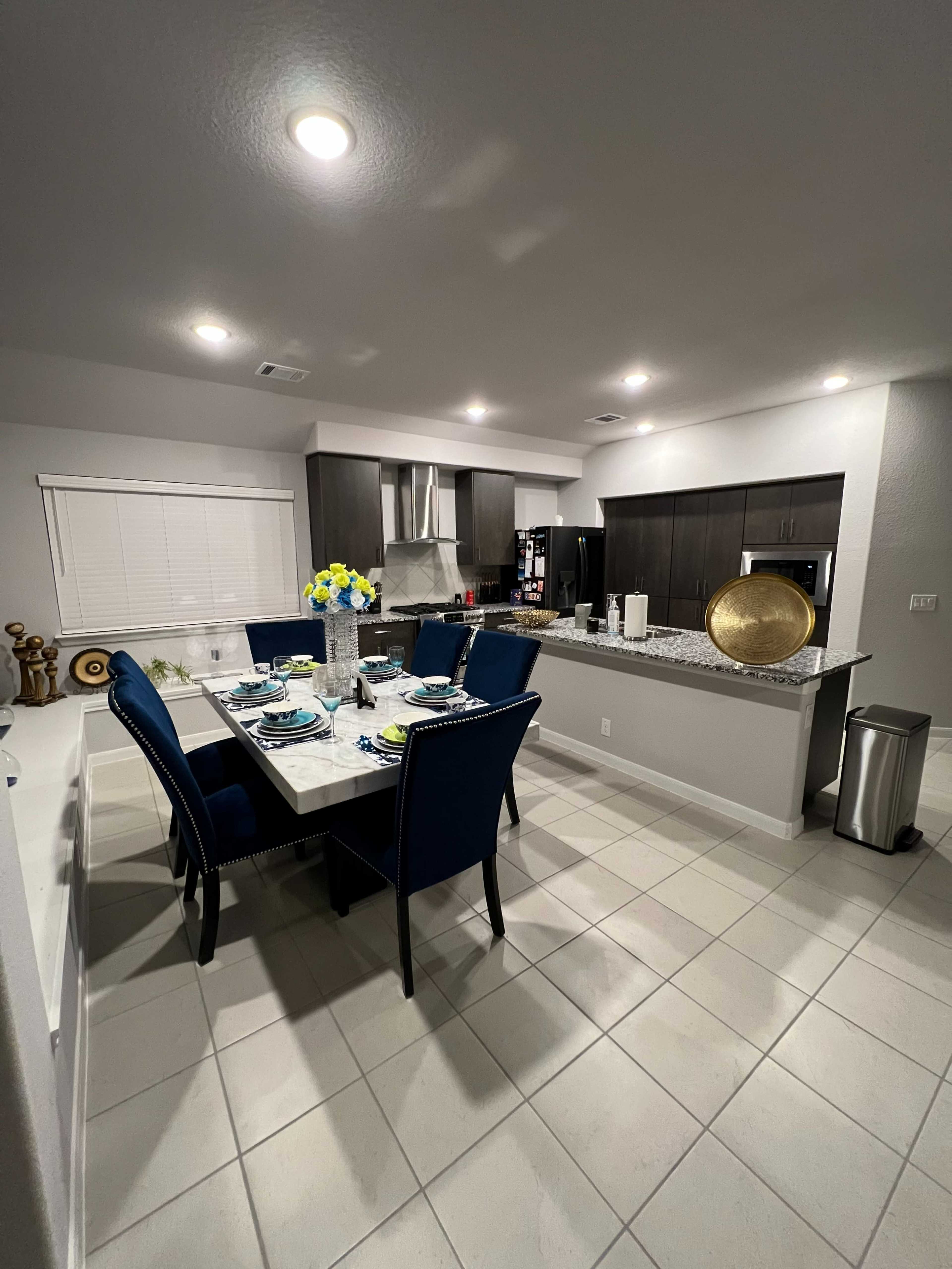 A modern kitchen and dining area with a table set for six, dark cabinets, and a countertop featuring decorative items.