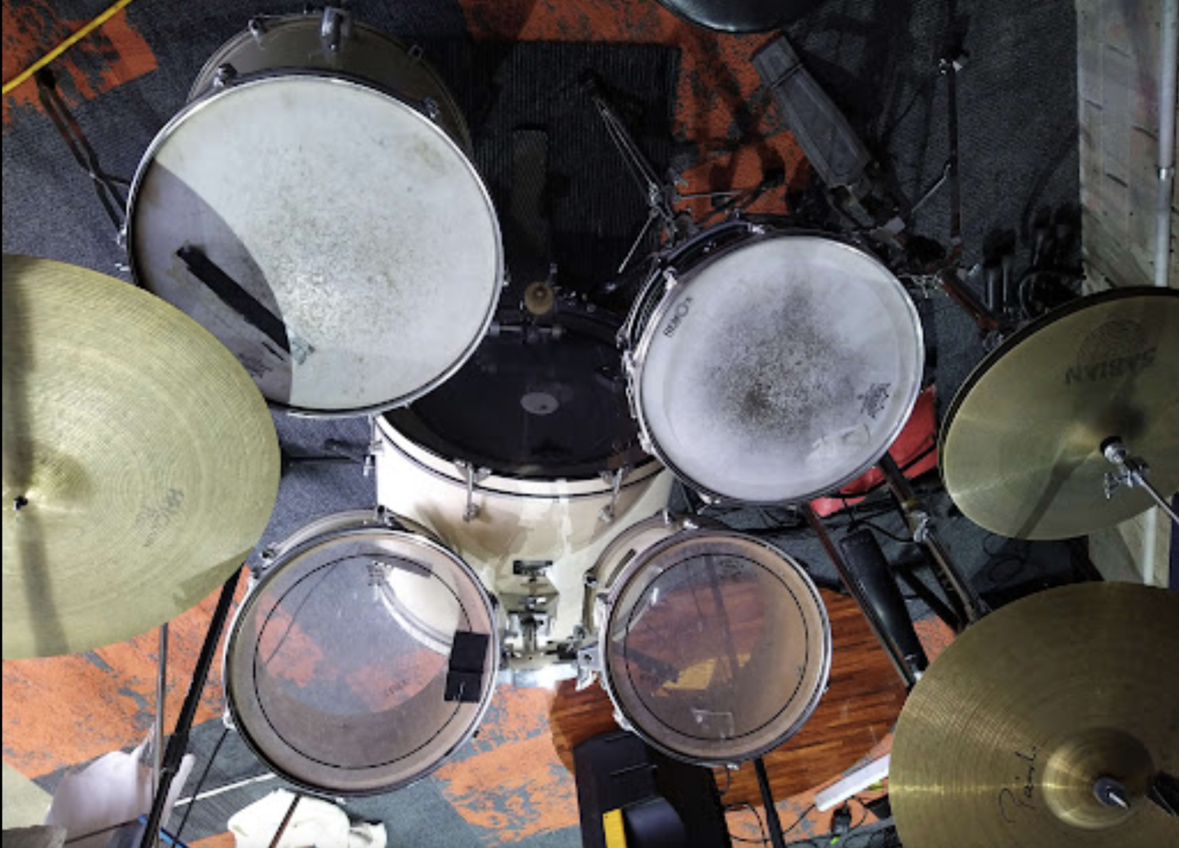 An overhead view of a drum set with several drums and cymbals positioned on a textured floor.