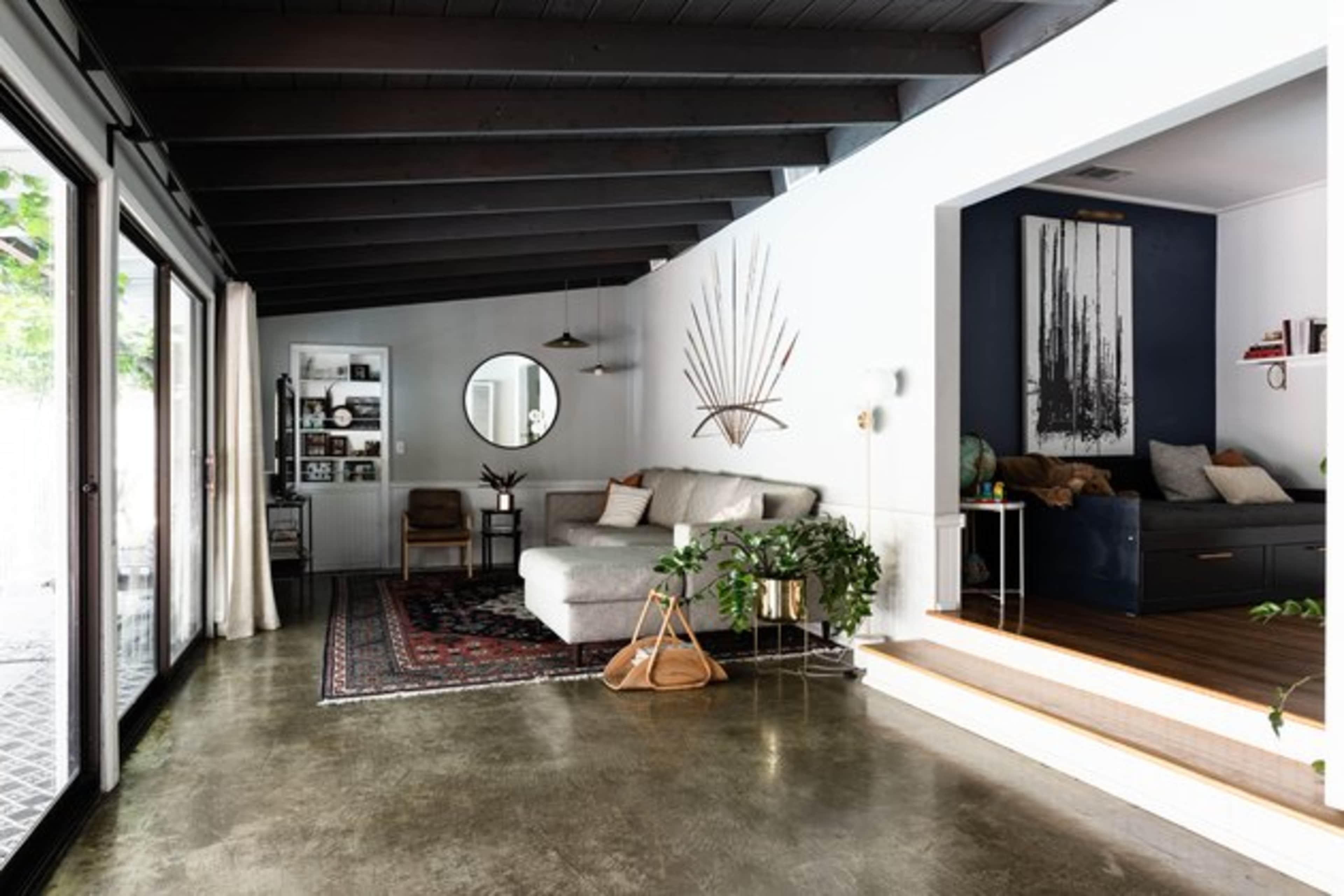 A modern living room with a sectional sofa, a round mirror, a dark accent wall, and large glass doors leading to an outdoor area.