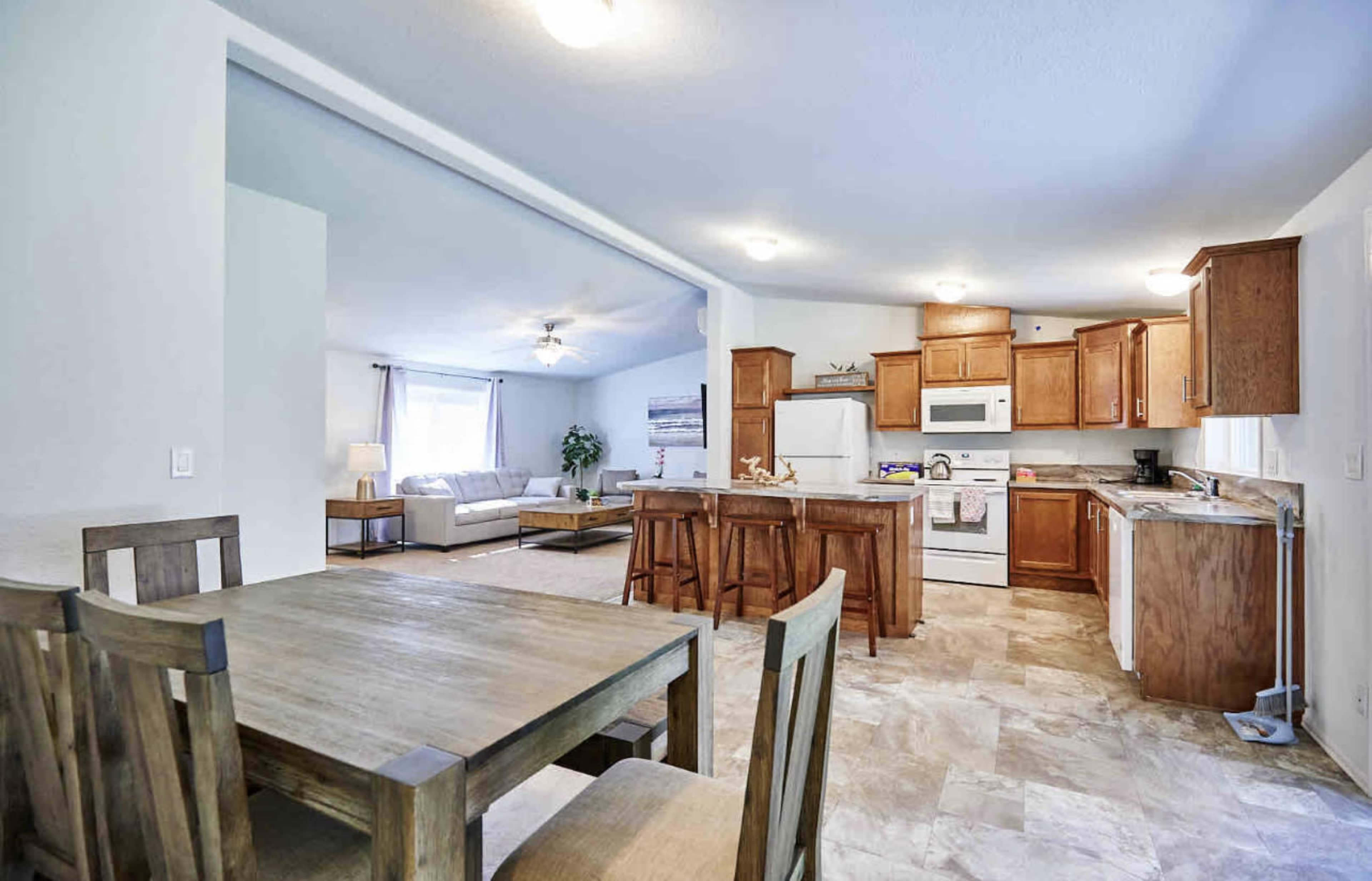 A bright, open kitchen and dining area with wooden cabinetry, a white refrigerator, and a dining table set for four.