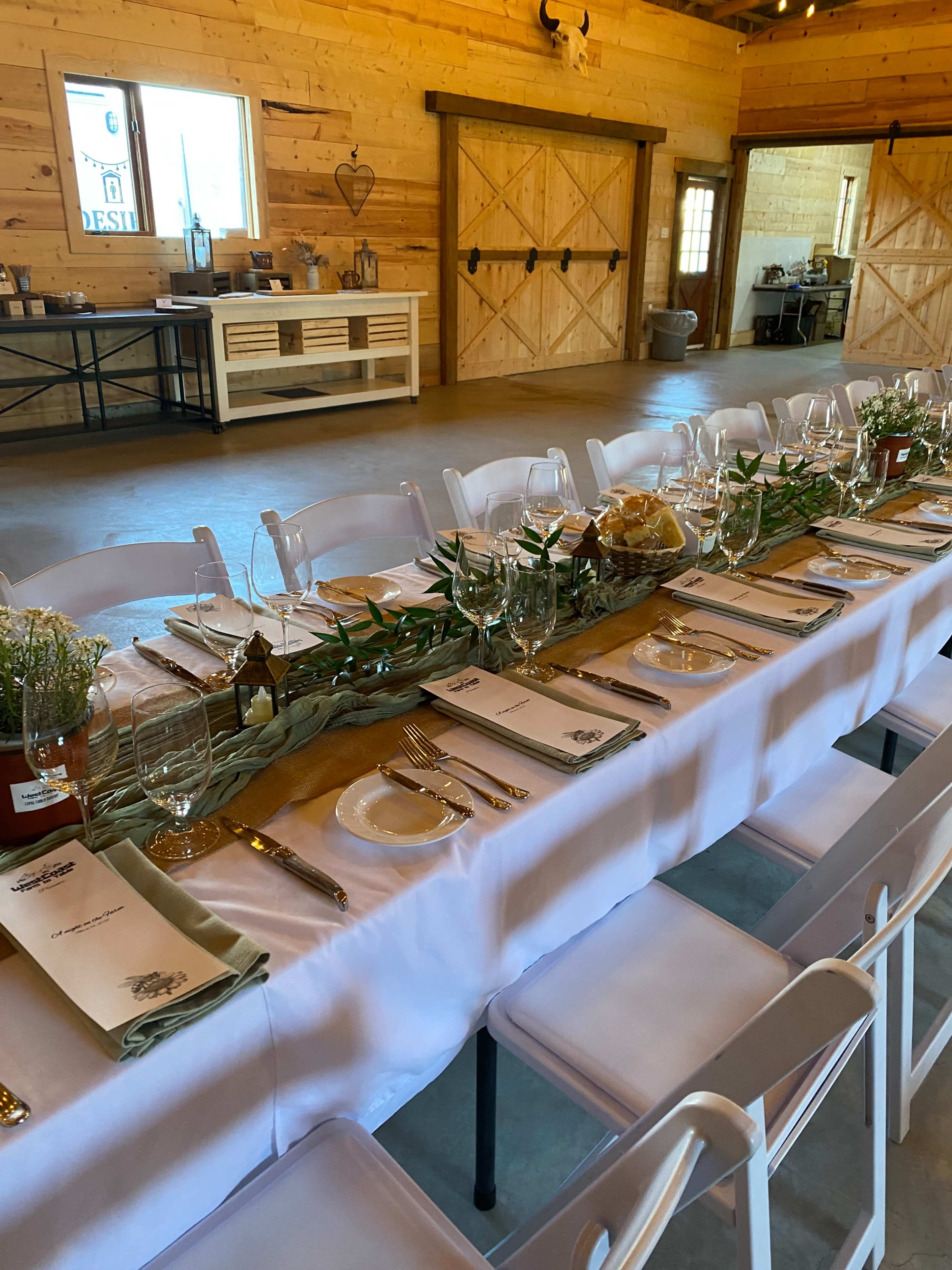 A long dining table is elegantly set with plates, glassware, and a decorative centerpiece in a rustic wooden venue.