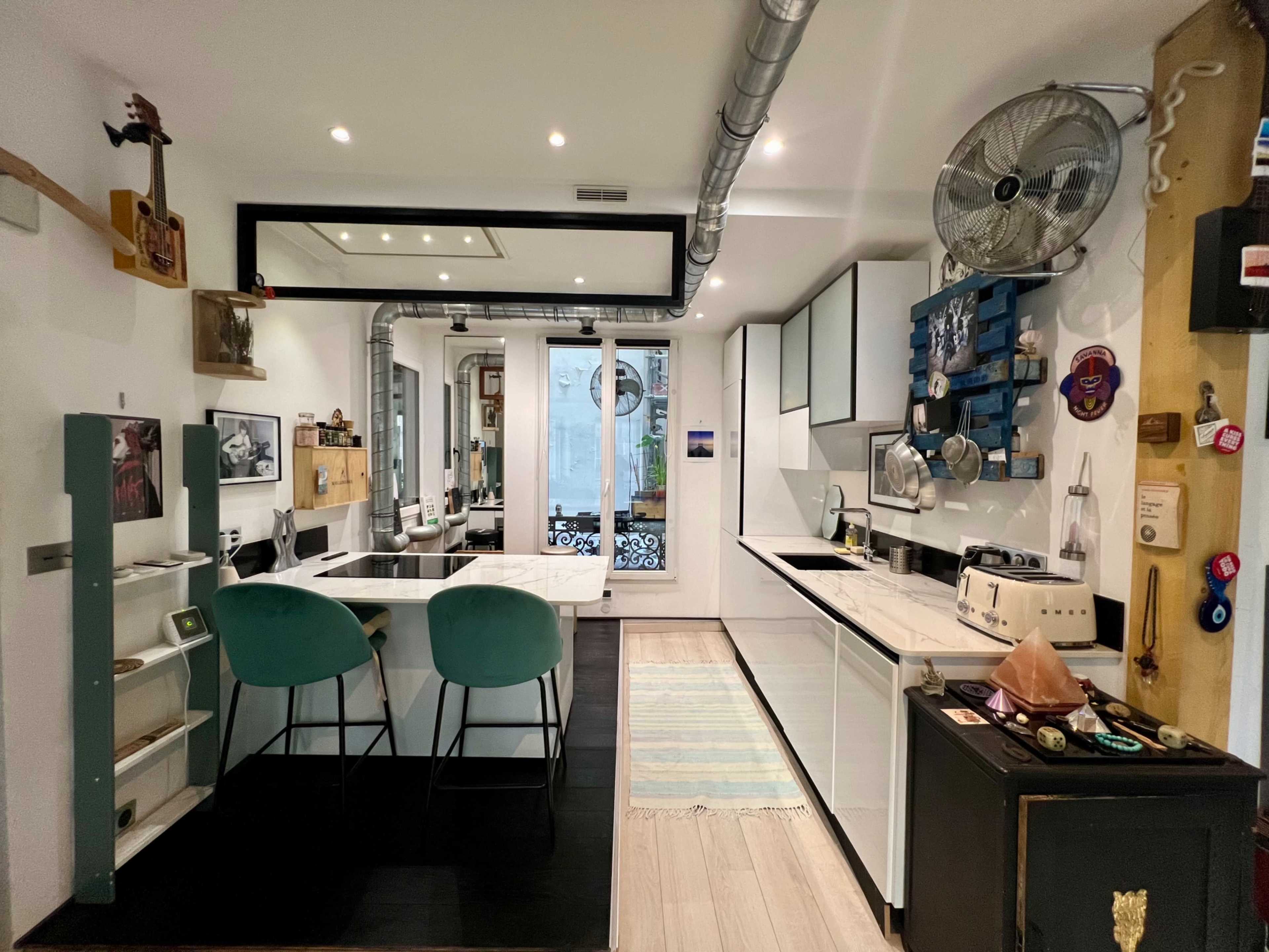 A modern kitchen with white cabinetry, a black and white color scheme, and two teal bar stools at a central island.