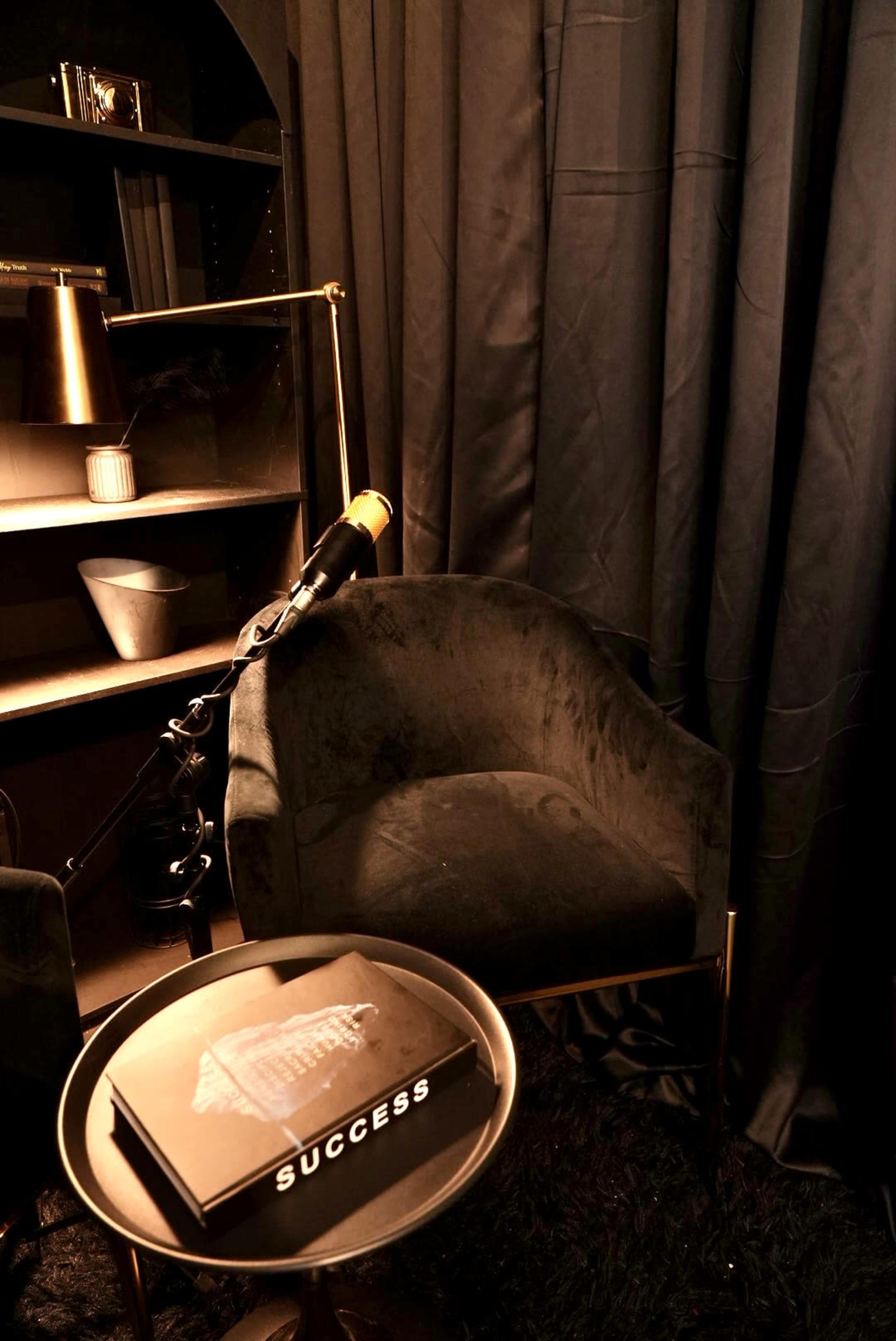 The image shows a cozy nook with a velvet chair, a small round table holding a book titled "SUCCESS," and dark curtains in the background.