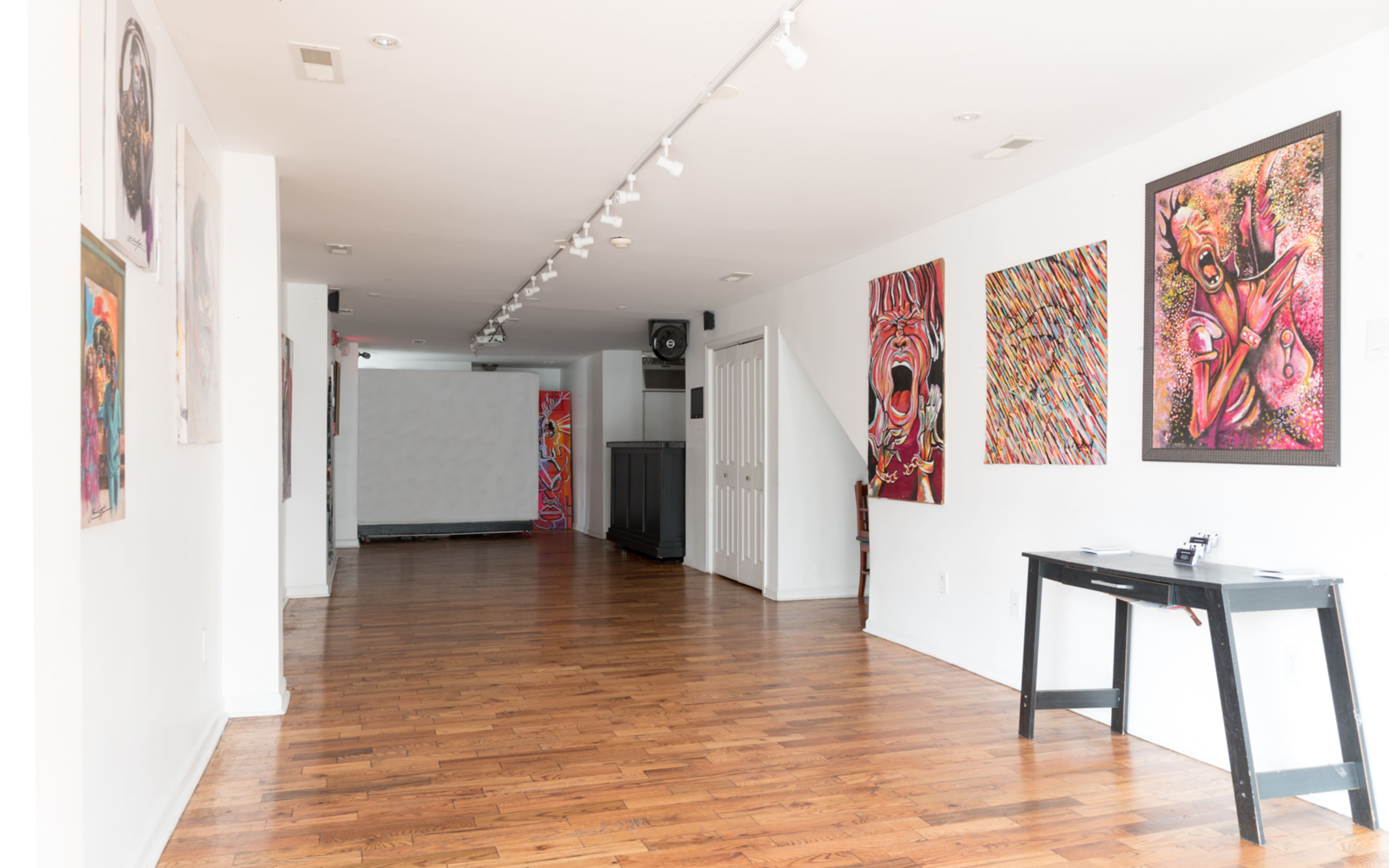 A spacious art gallery with colorful paintings on the walls and wooden flooring.