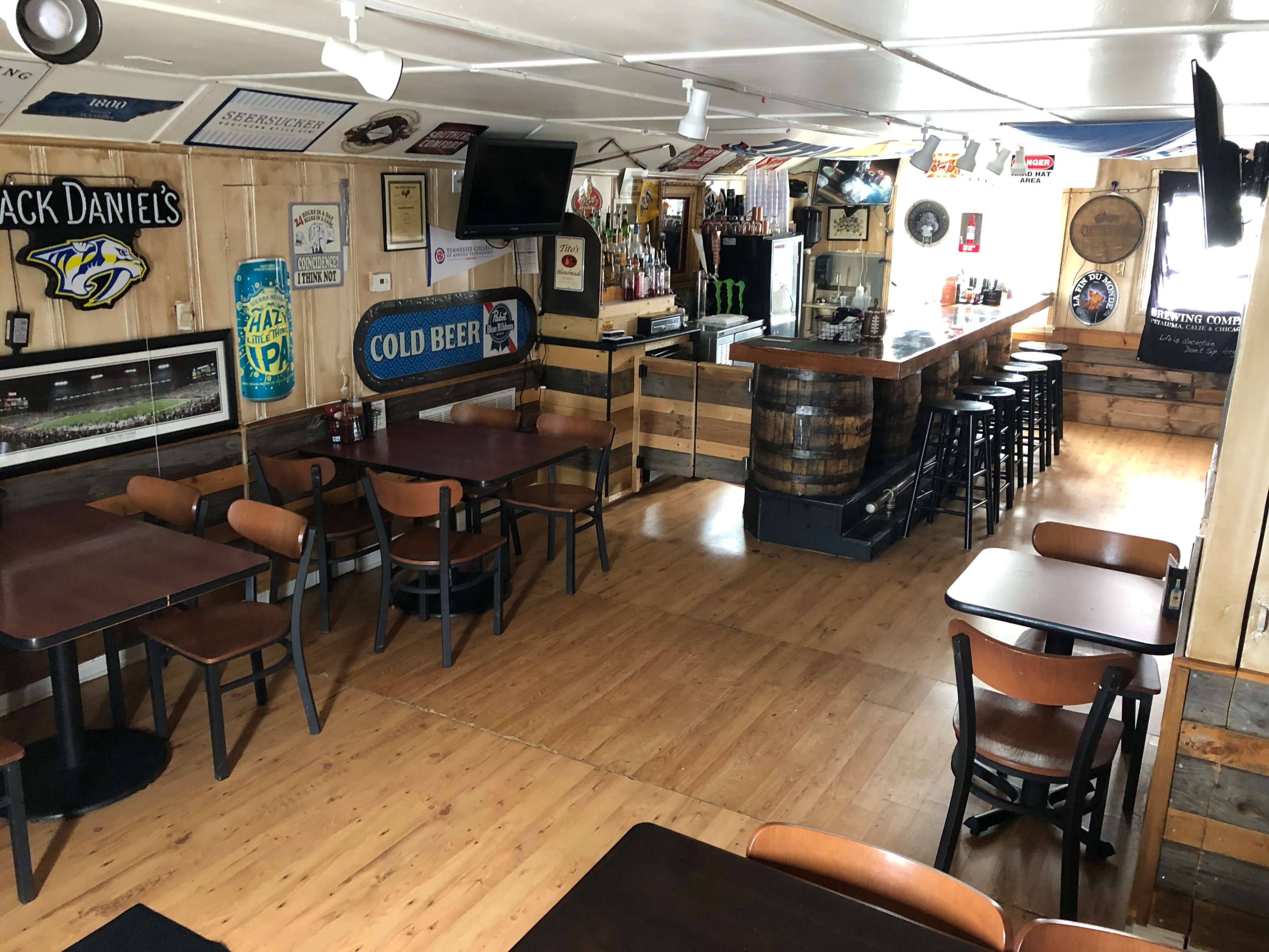 A rustic bar interior with wooden tables, chairs, a long bar counter, and various signs and decorations on the walls.