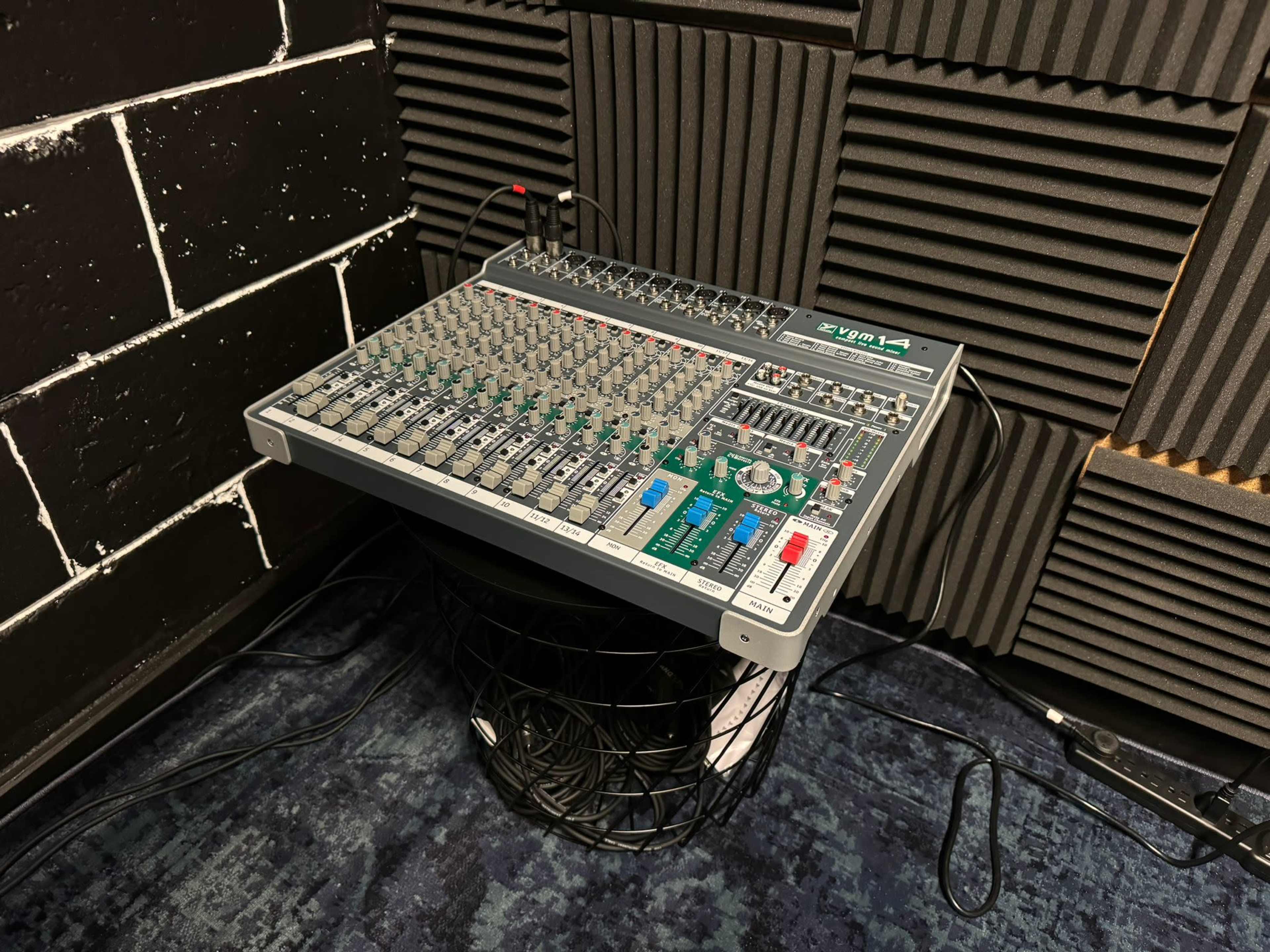 A mixer console is placed on top of a wire basket in a soundproofed room with textured black walls.