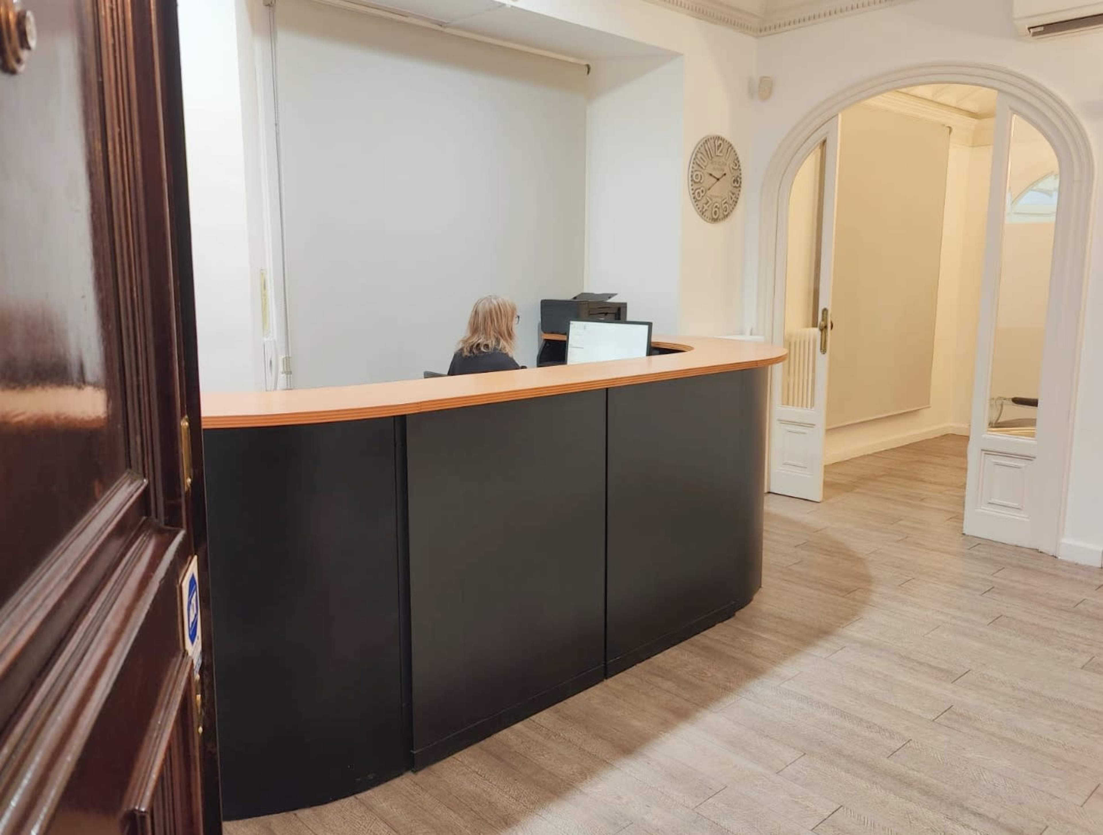 A reception desk with a computer is shown, and a person is seated at the desk in an office environment.
