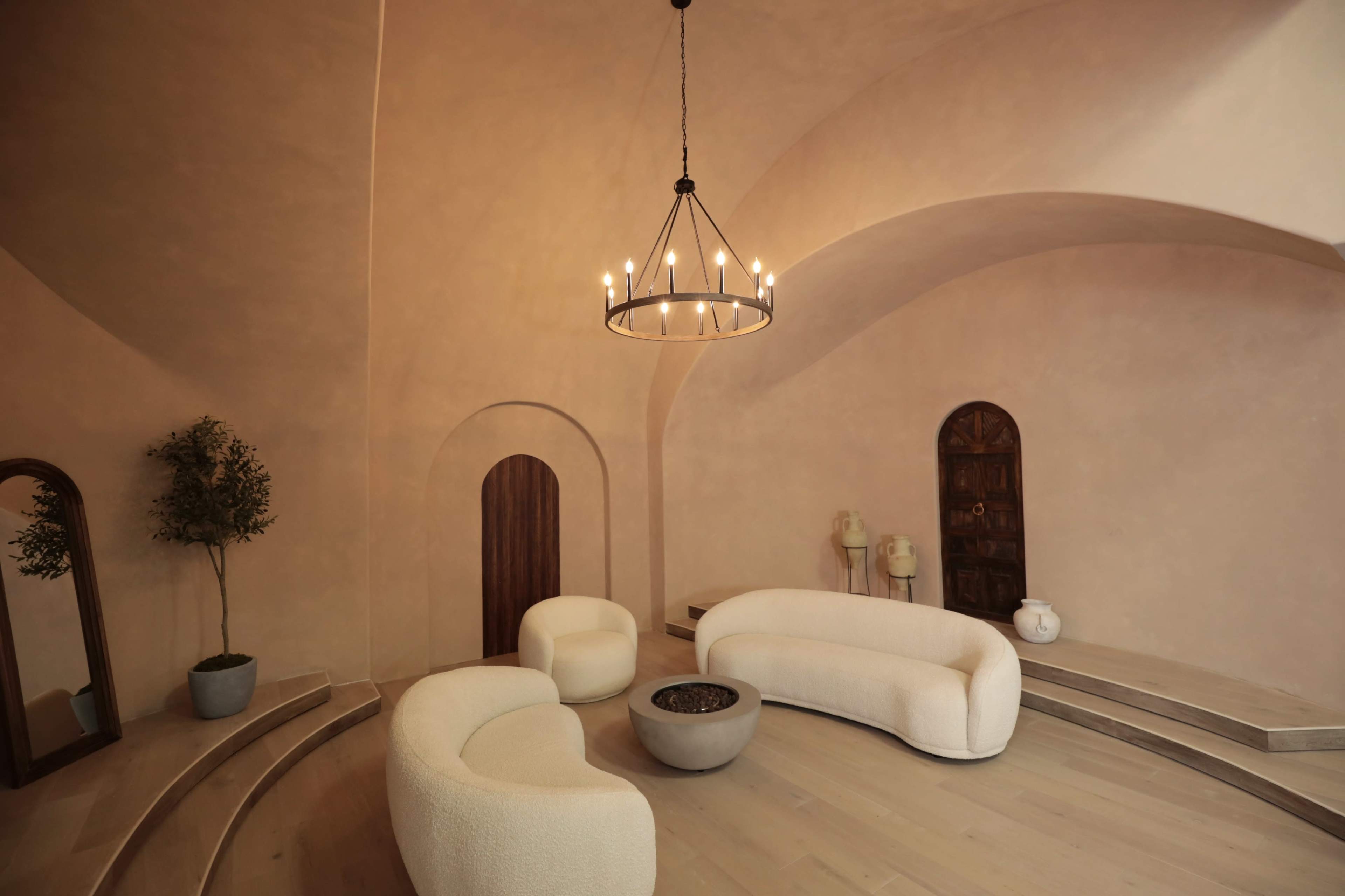 A minimalist, curved seating arrangement surrounding a central fire pit in a softly lit, arched room with neutral-toned walls.