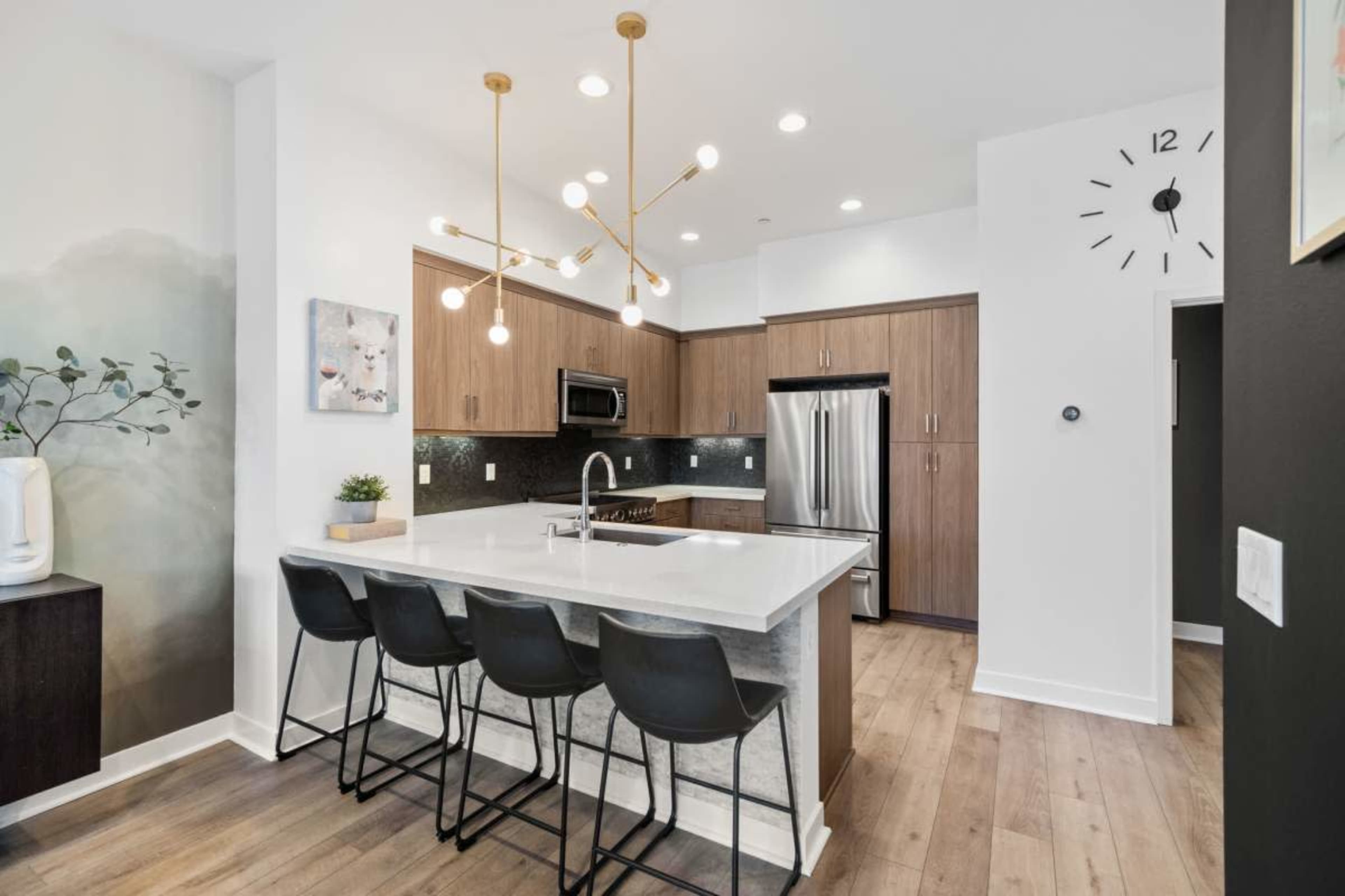 A modern kitchen featuring a large island with four black bar stools, stainless steel appliances, and pendant lighting.