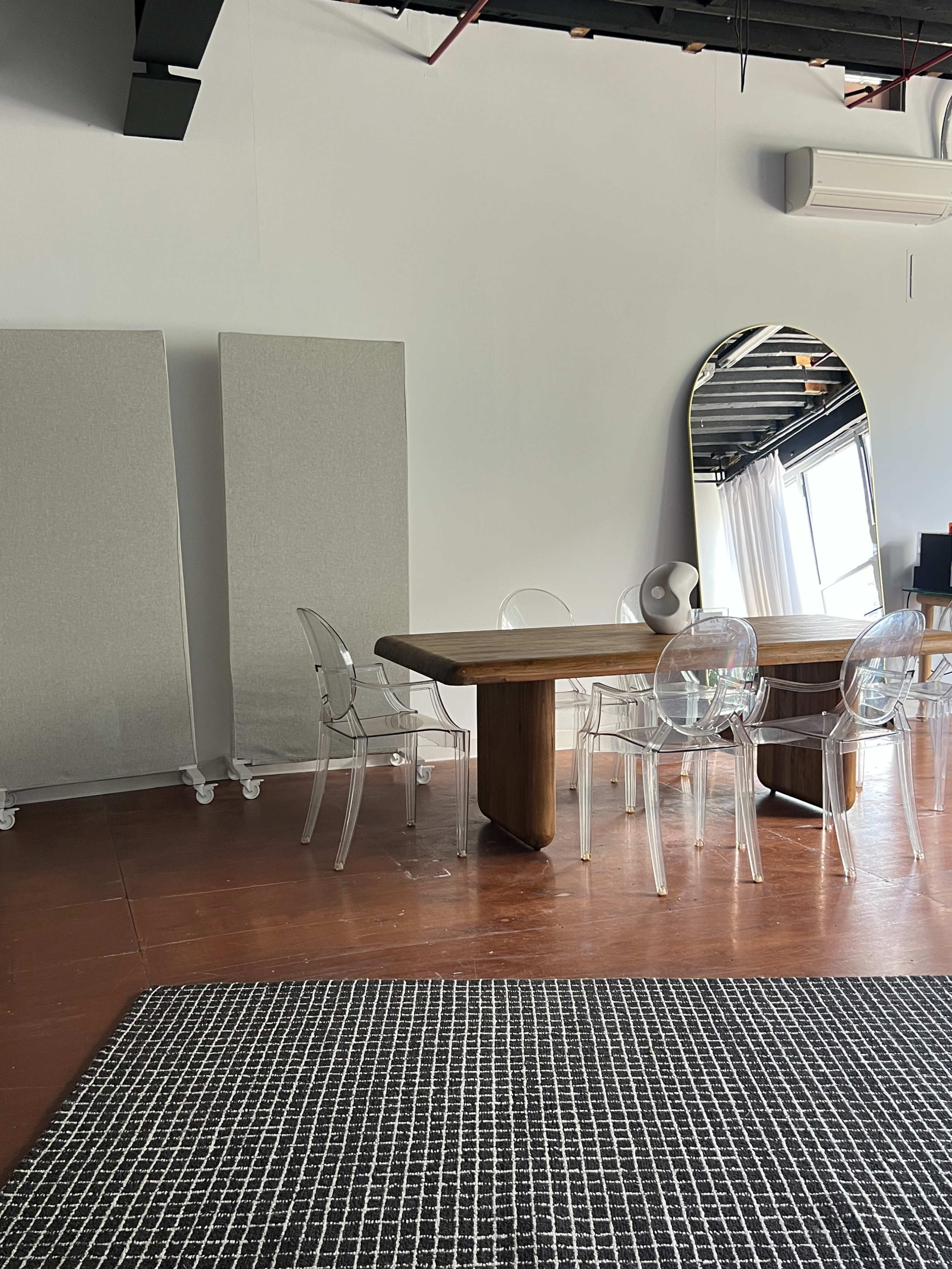 The image shows a modern conference room with a wooden table, transparent chairs, a large mirror, and two fabric panels on the wall.