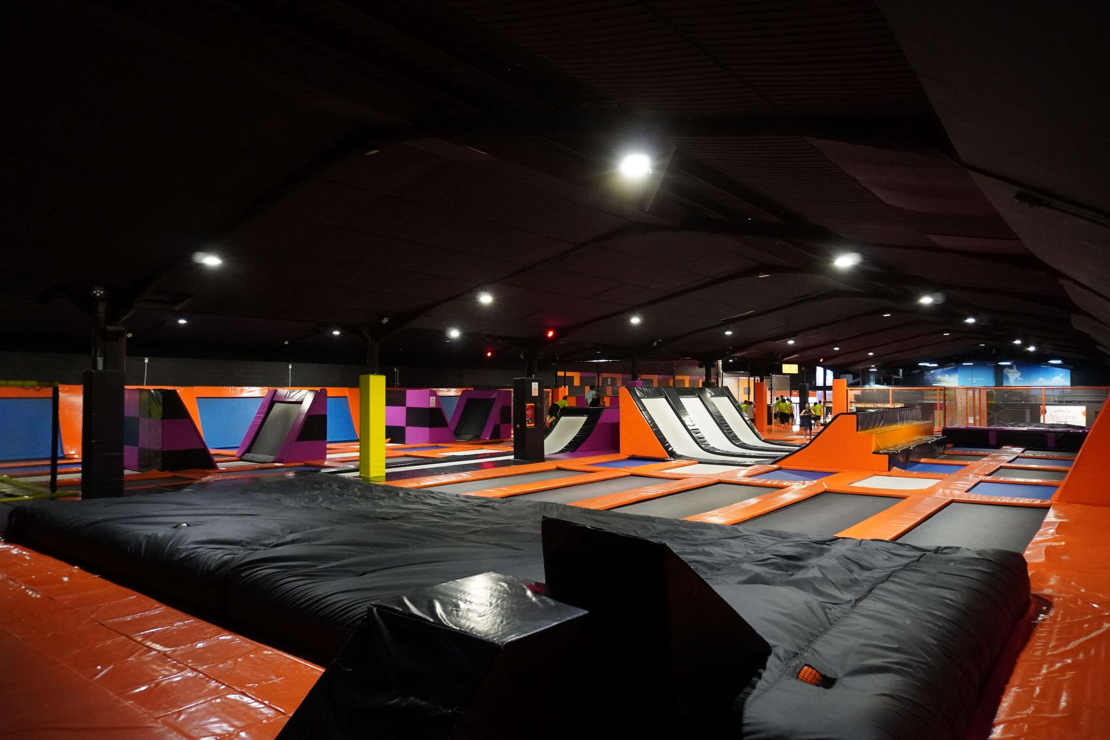 A large indoor trampoline park with multiple trampolines, foam pits, and an open play area under low lighting.