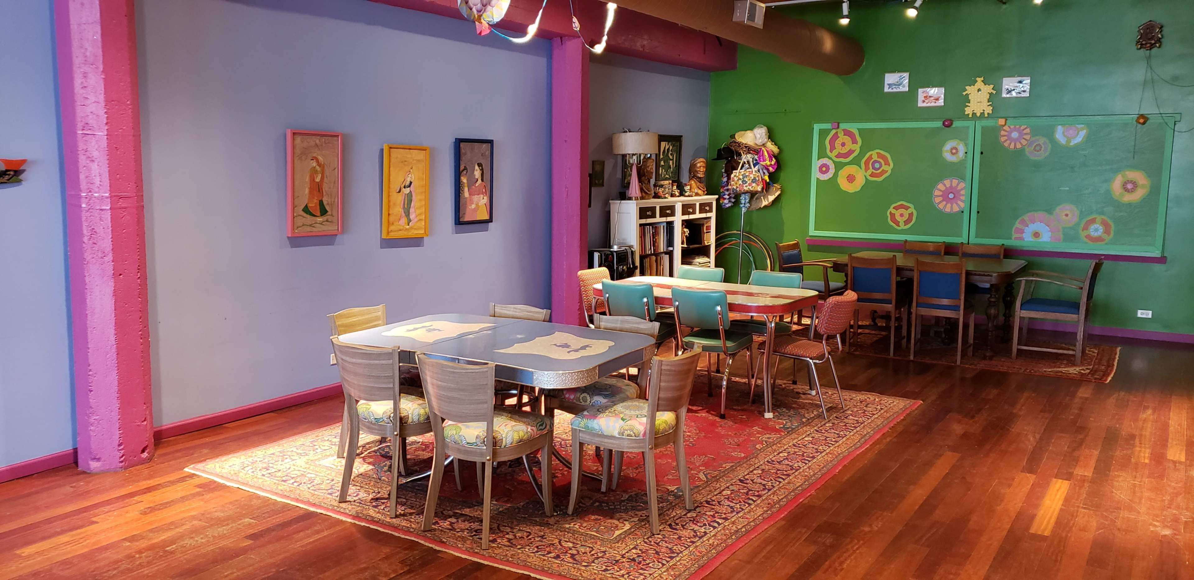 The room features a colorful decor with a mix of chairs and tables arranged on a wooden floor, surrounded by vibrant wall colors and artwork.