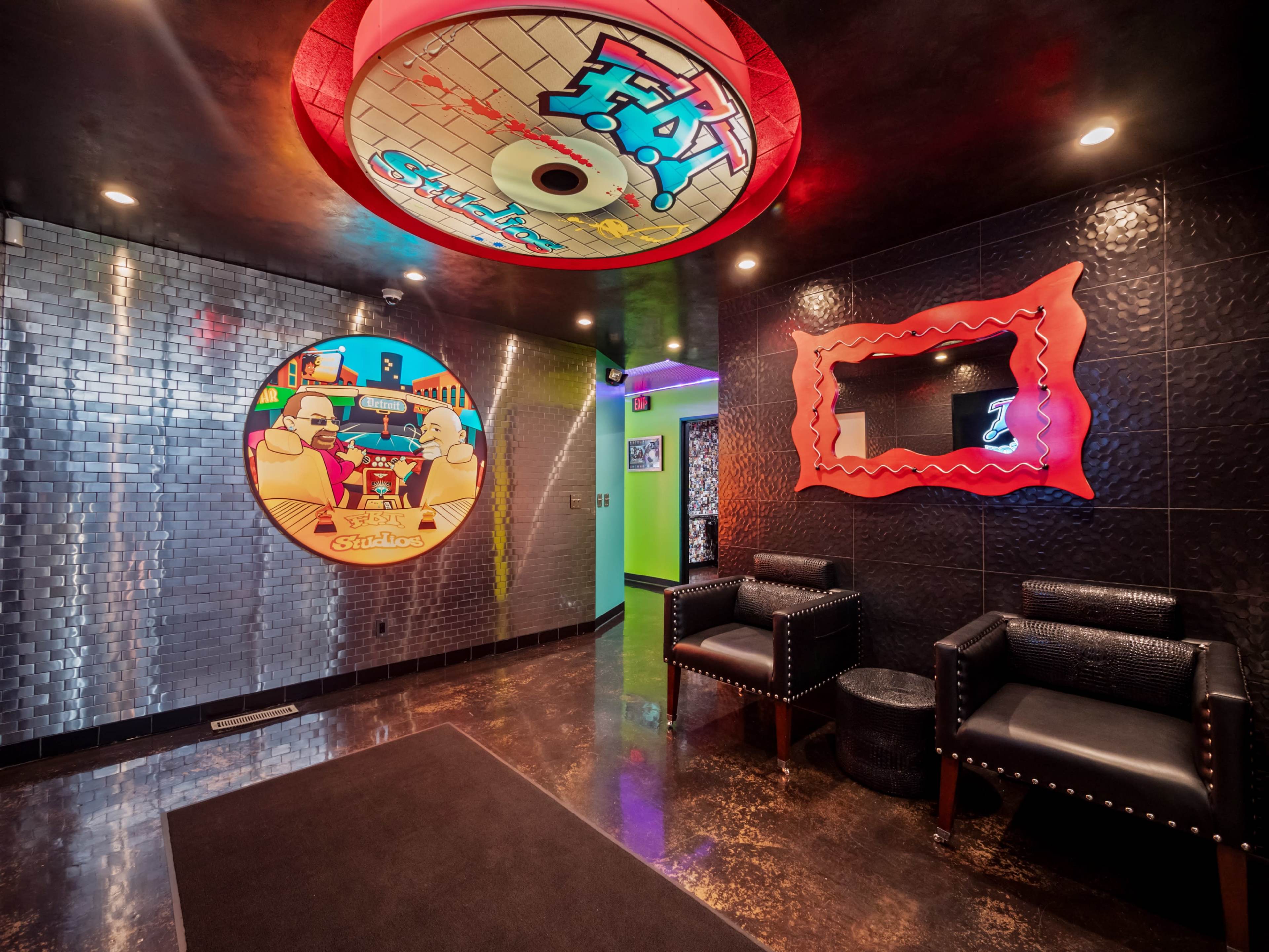 The image shows a modern hallway with colorful wall art, textured black walls, and two black chairs in a contemporary design.