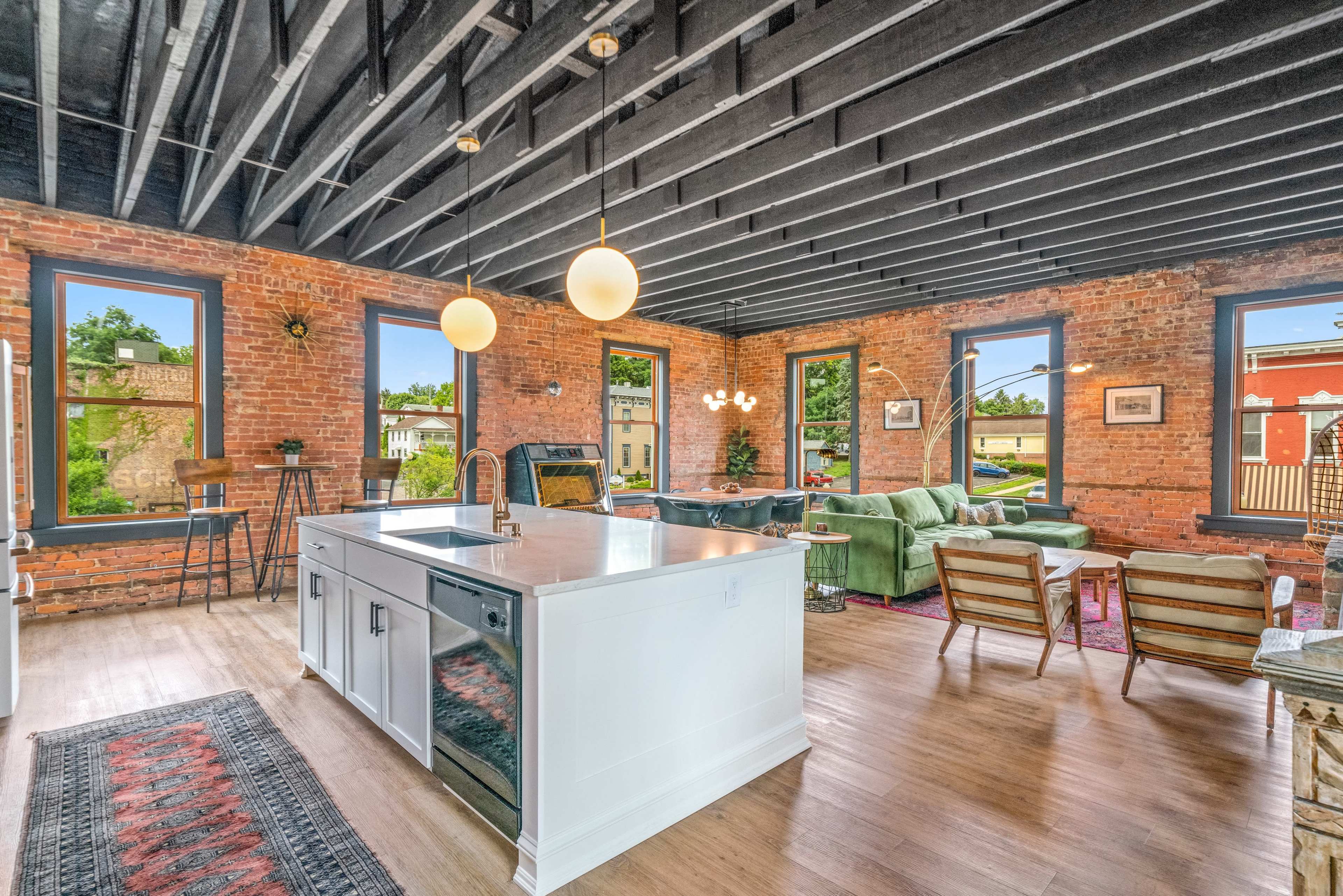 A spacious open-concept living area with a kitchen island, exposed brick walls, and large windows letting in natural light.