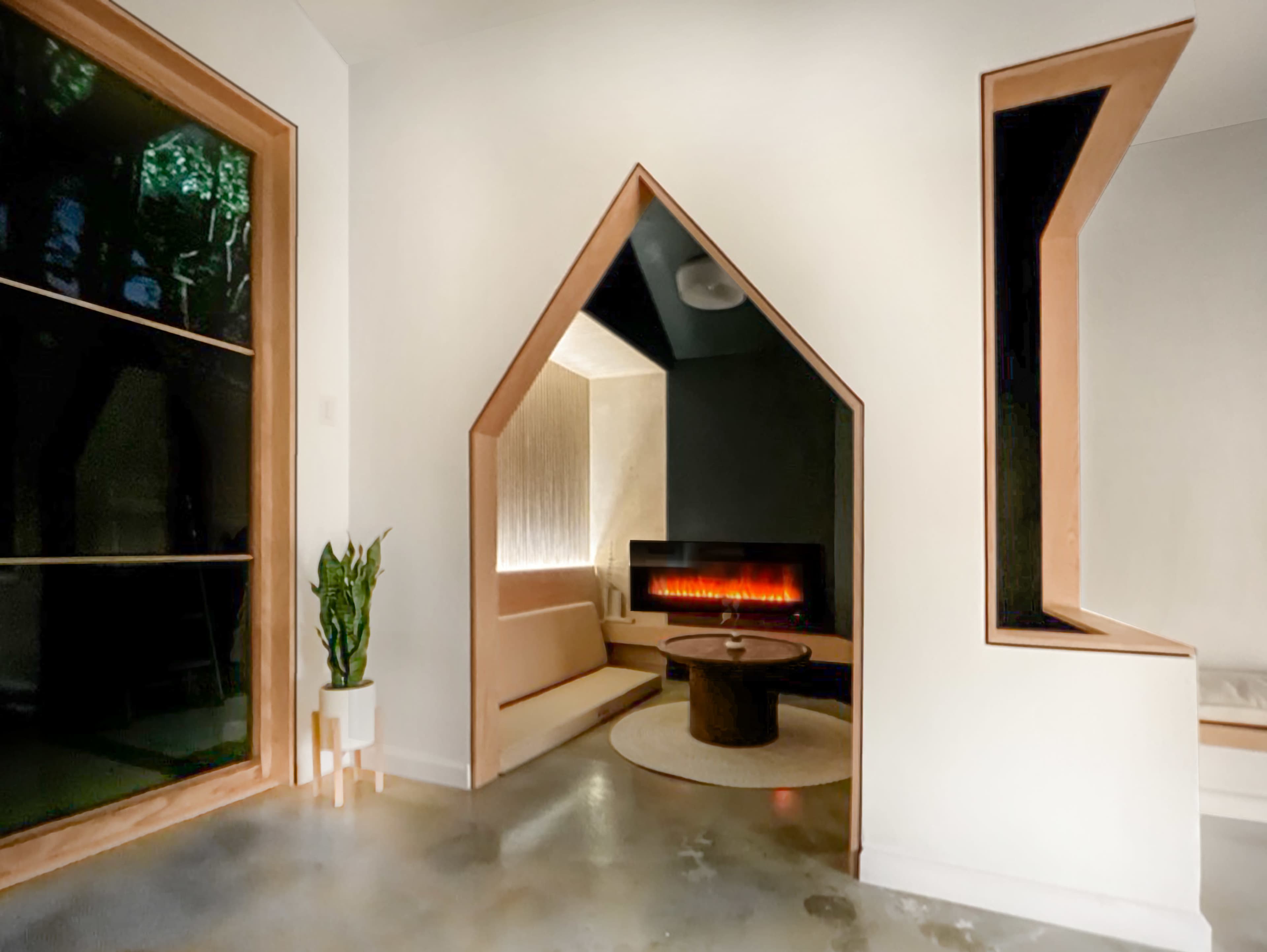 A minimalist living space features angular architecture with a modern fireplace and a soft seating area illuminated by natural light.