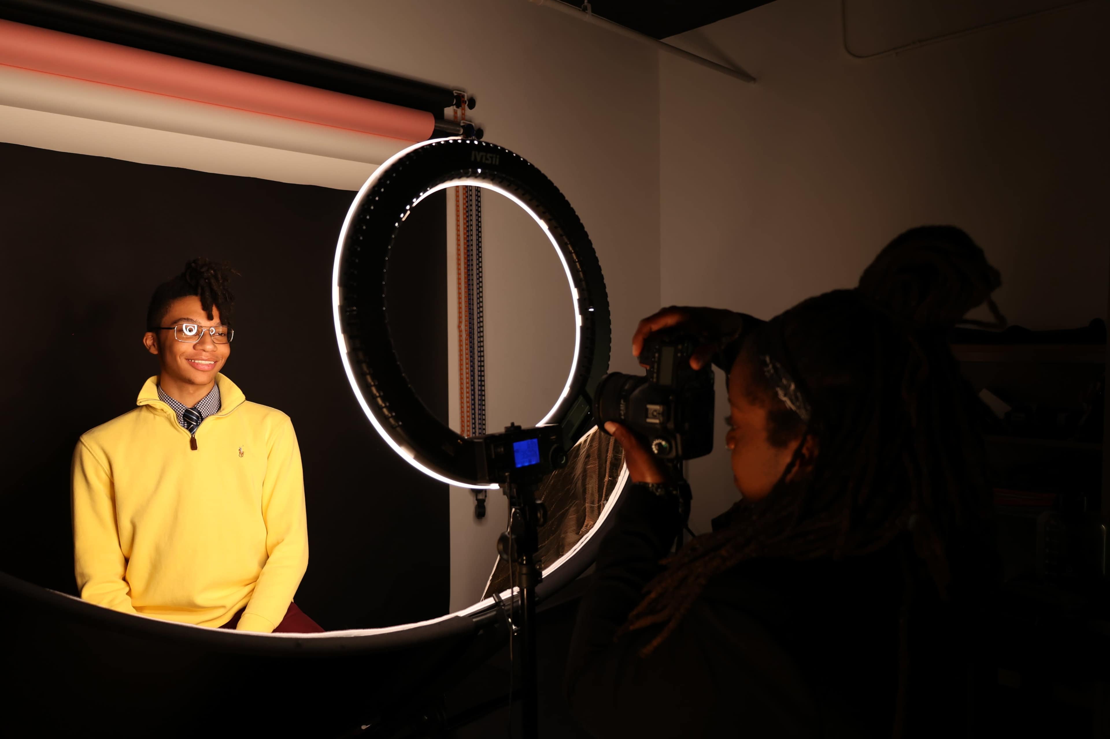 A photographer captures an image of a smiling subject in front of a ring light in a studio setting.