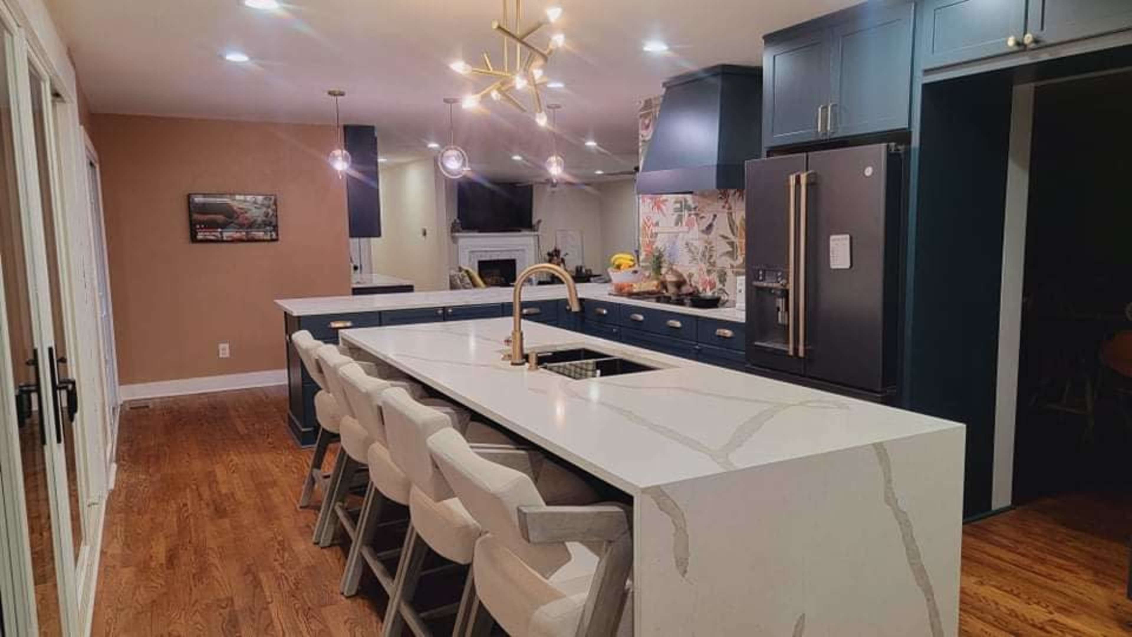 A modern kitchen featuring a large white countertop island with seating, blue cabinetry, and pendant lighting.