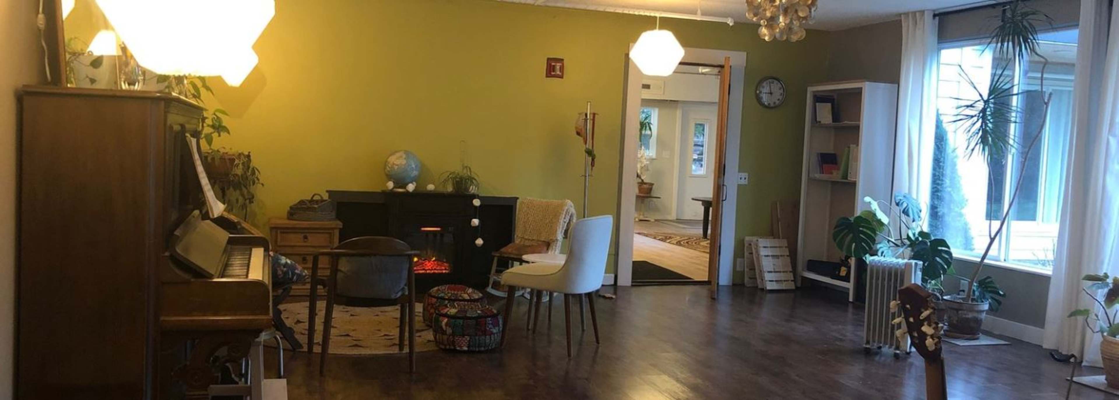 A spacious living room with a green accent wall, a piano, a globe on a stand, and various plants around the area.