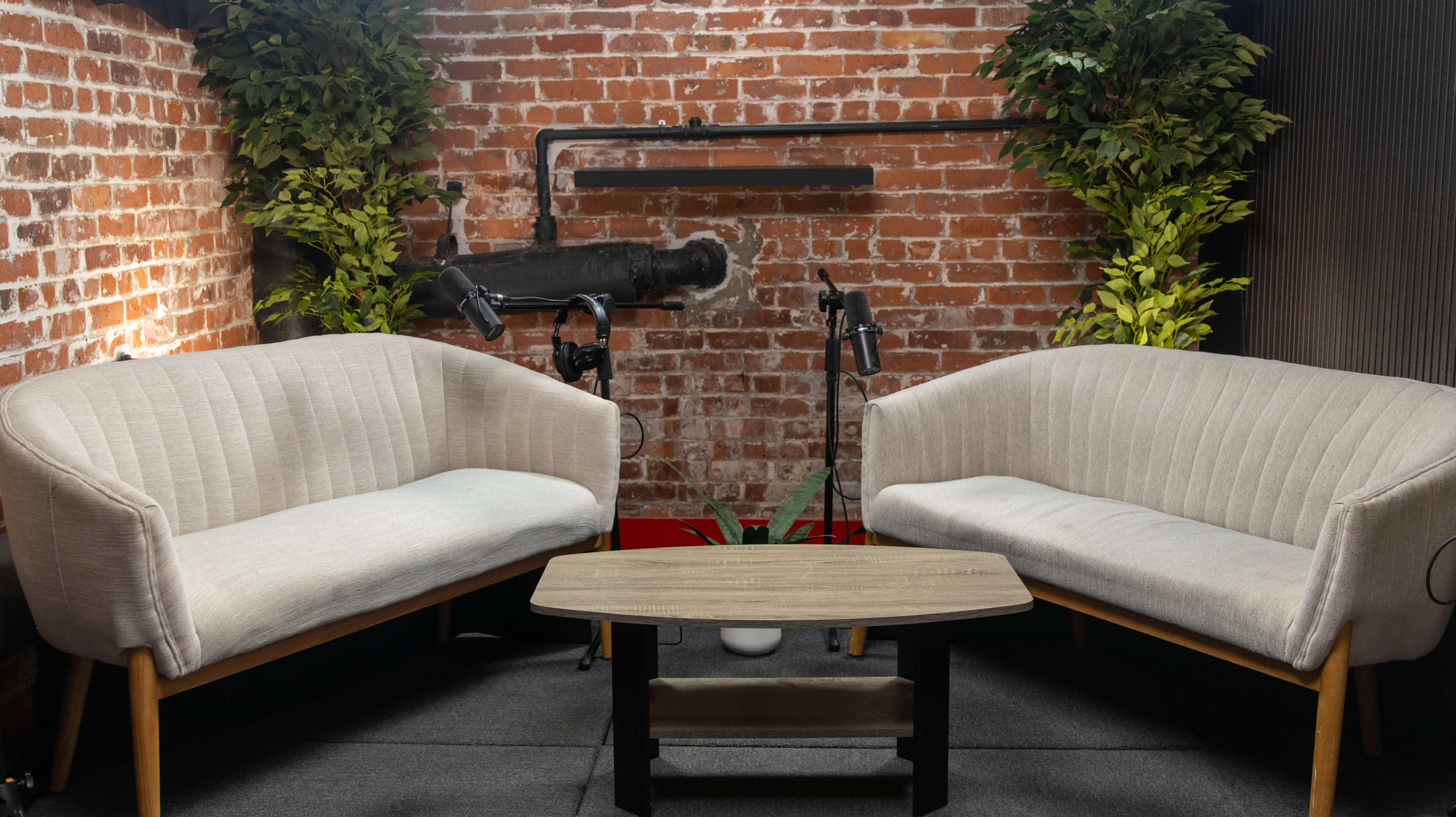 The image depicts a cozy seating area with two pale sofas facing each other, a small table in between, and a backdrop of exposed brick walls and greenery.