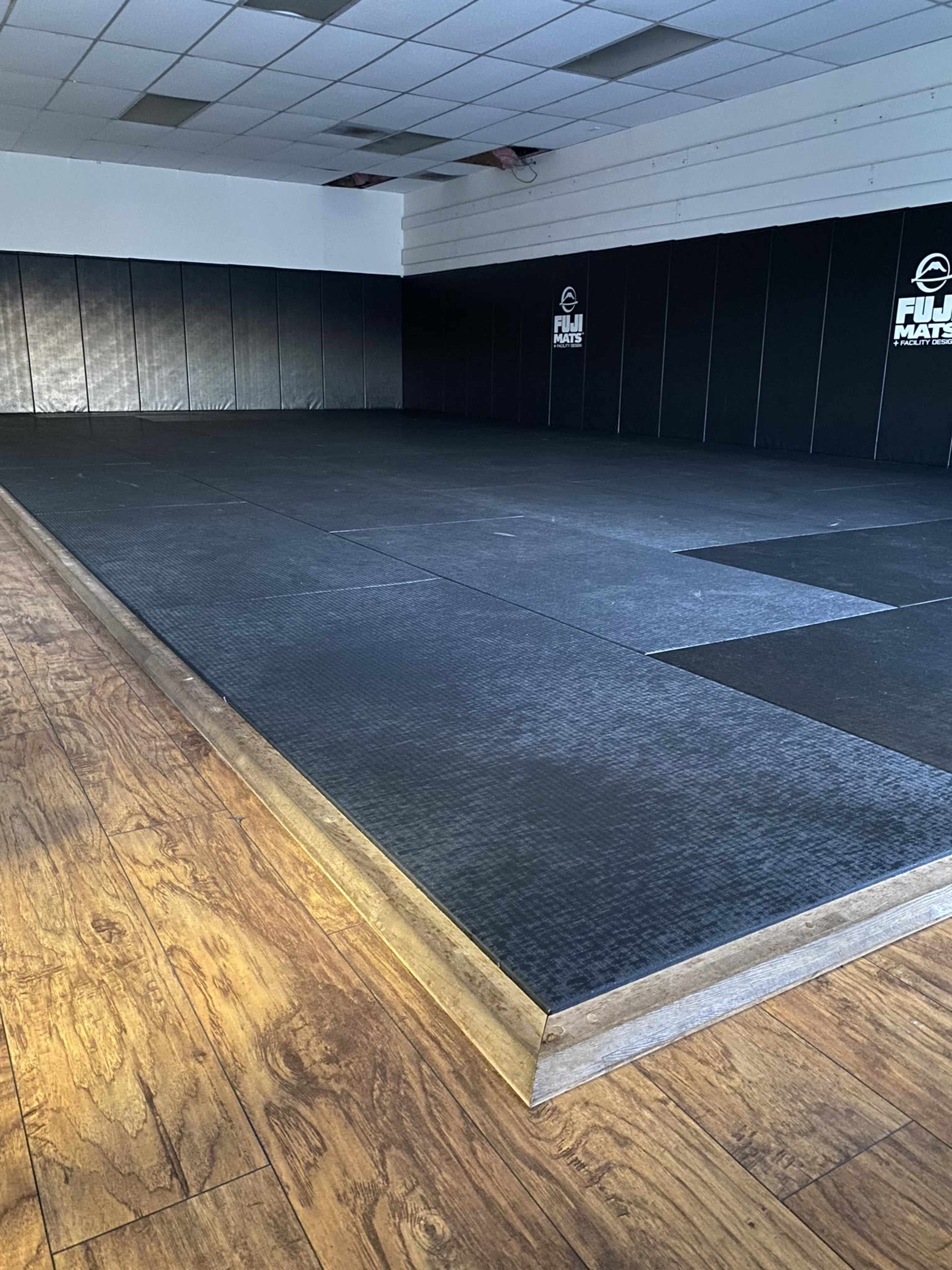A martial arts training space with black padded mats and wooden flooring.