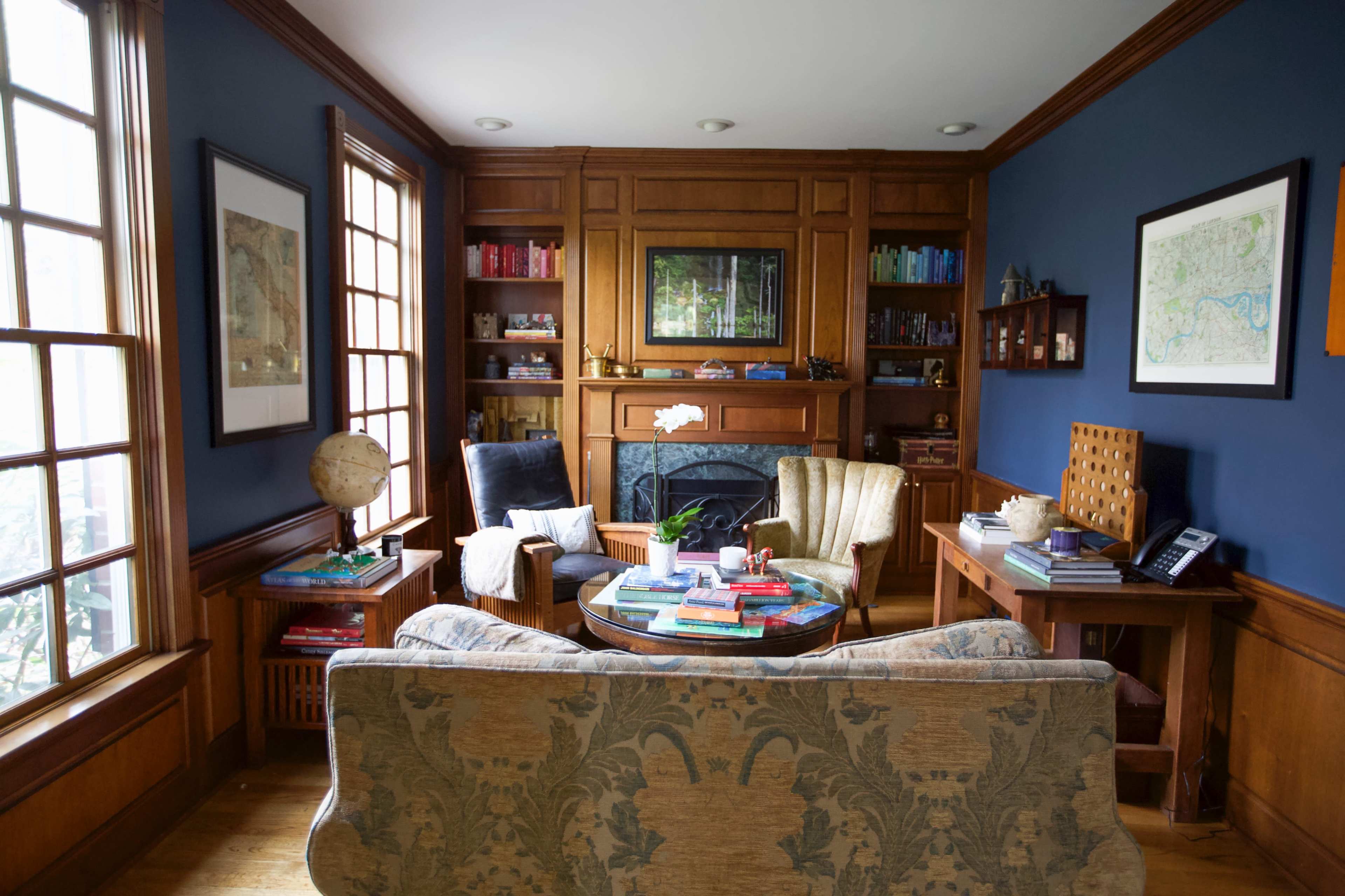 A cozy living room with hardwood accents, a fireplace, bookshelves filled with books, and two armchairs arranged around a coffee table.