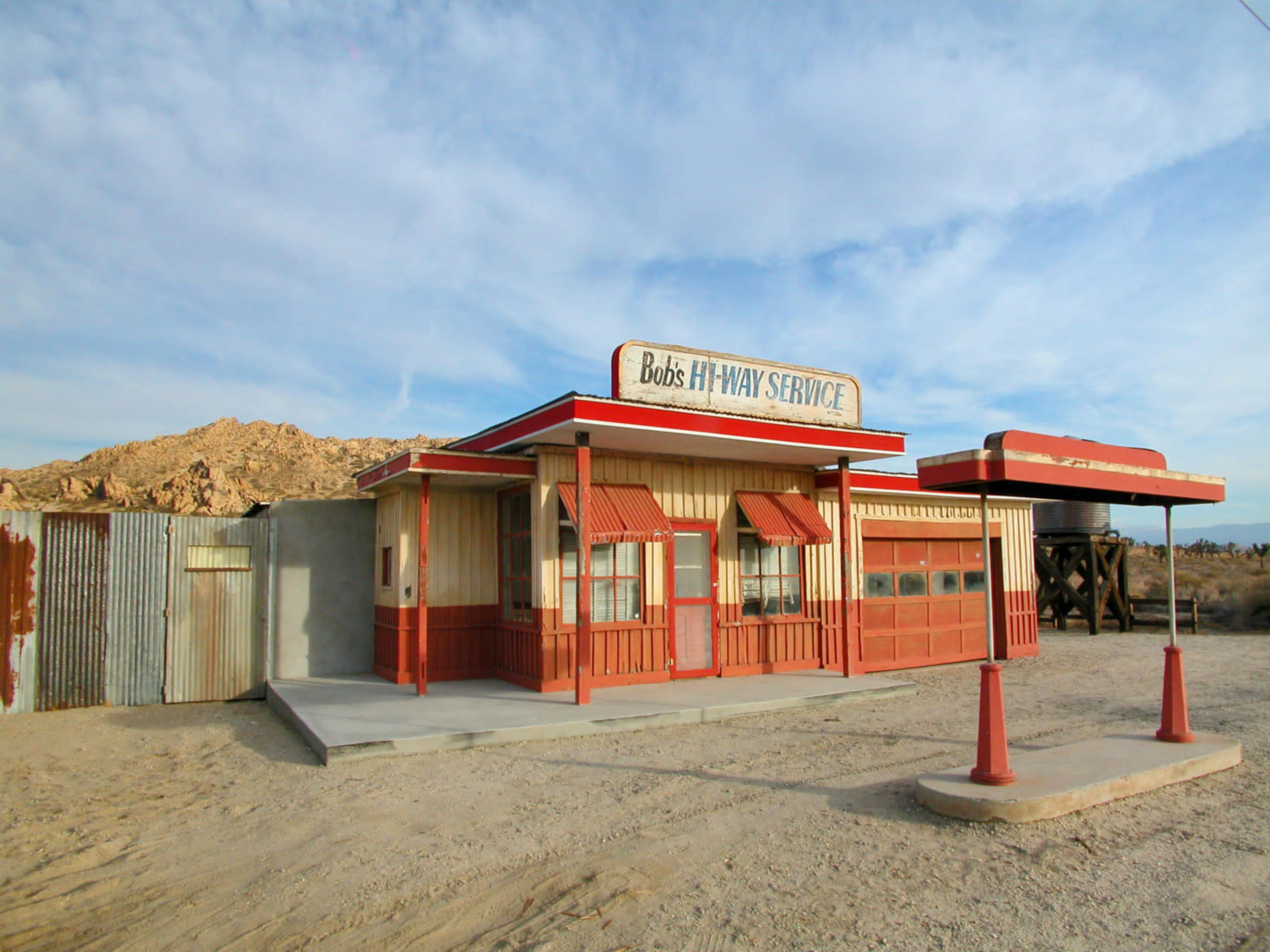 The image shows an old, rustic gas station with a red and white exterior set against a barren desert landscape.