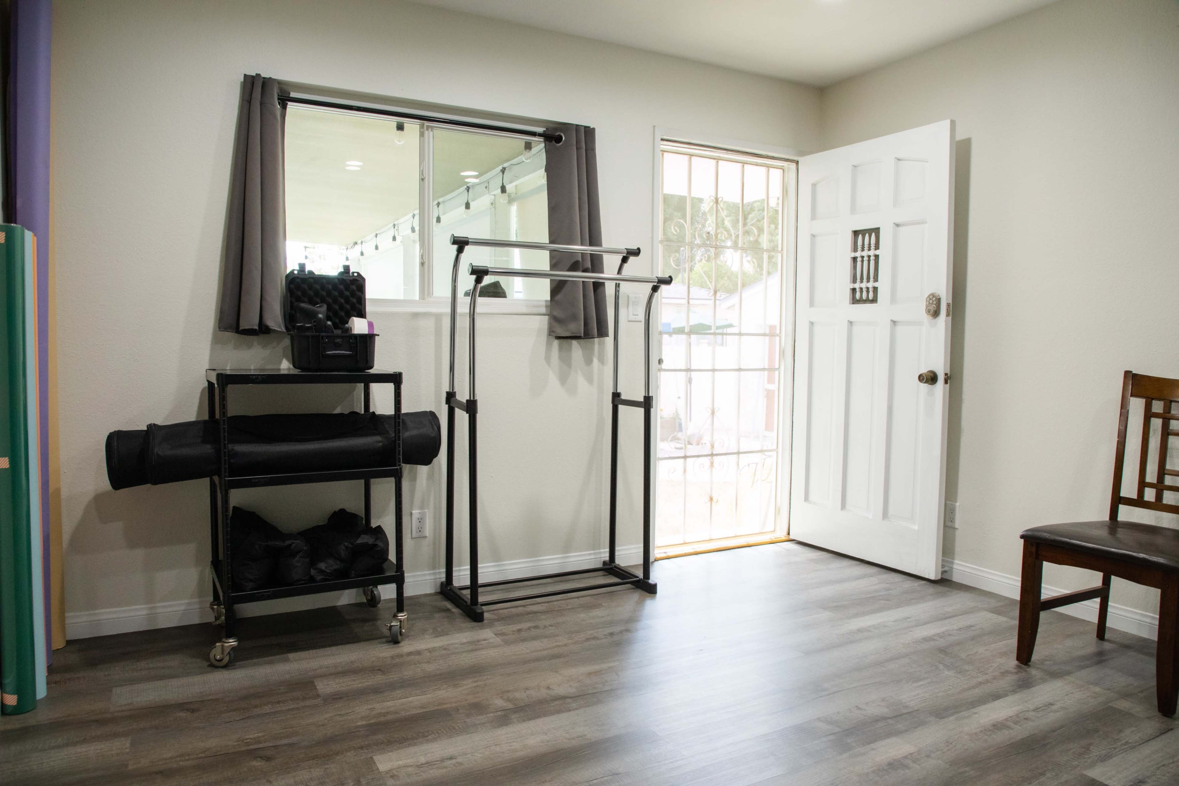 A minimalistic room with a door leading outside, a clothing rack on wheels, and a chair in the corner.