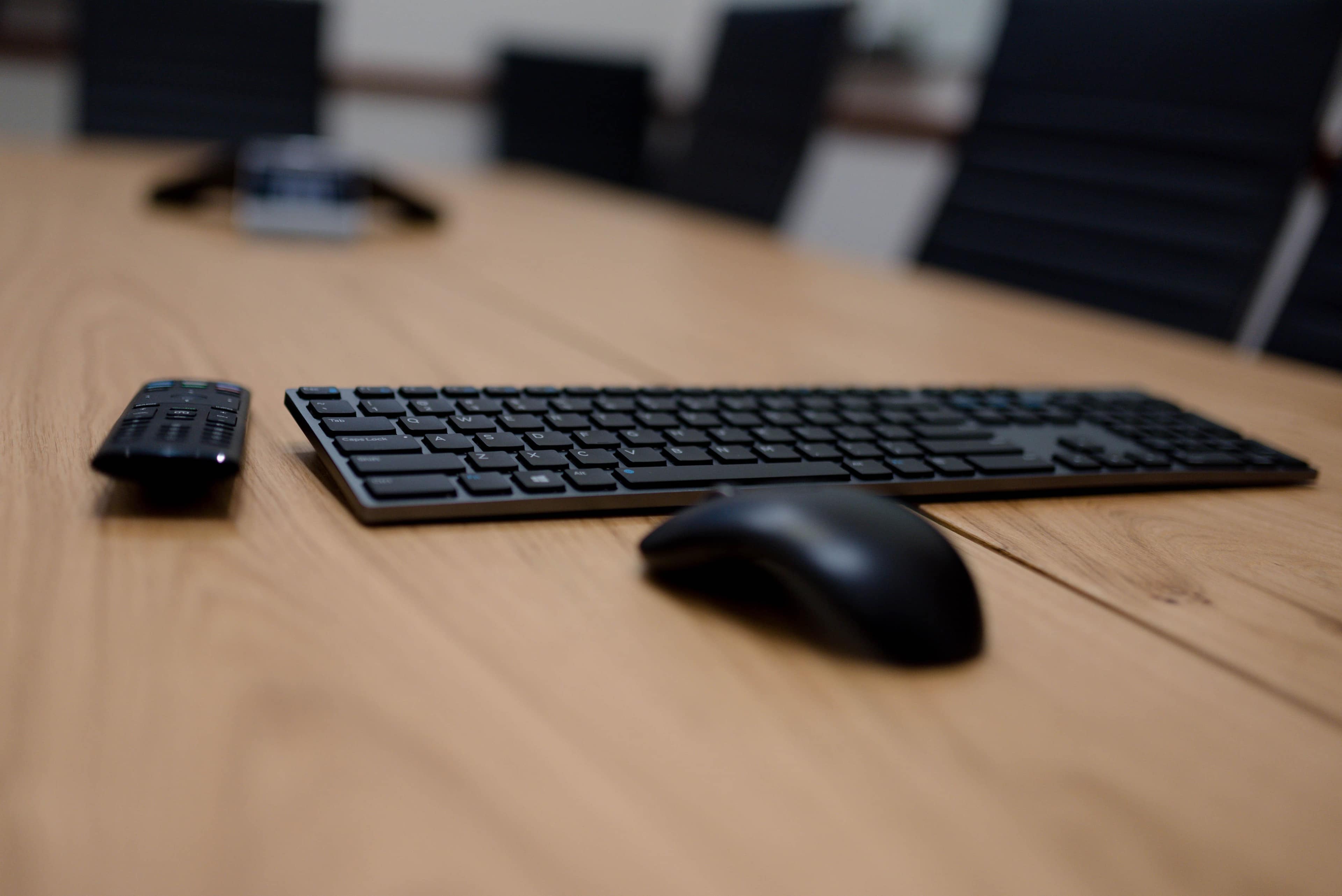 A black keyboard and mouse are positioned on a wooden conference table next to a remote control.