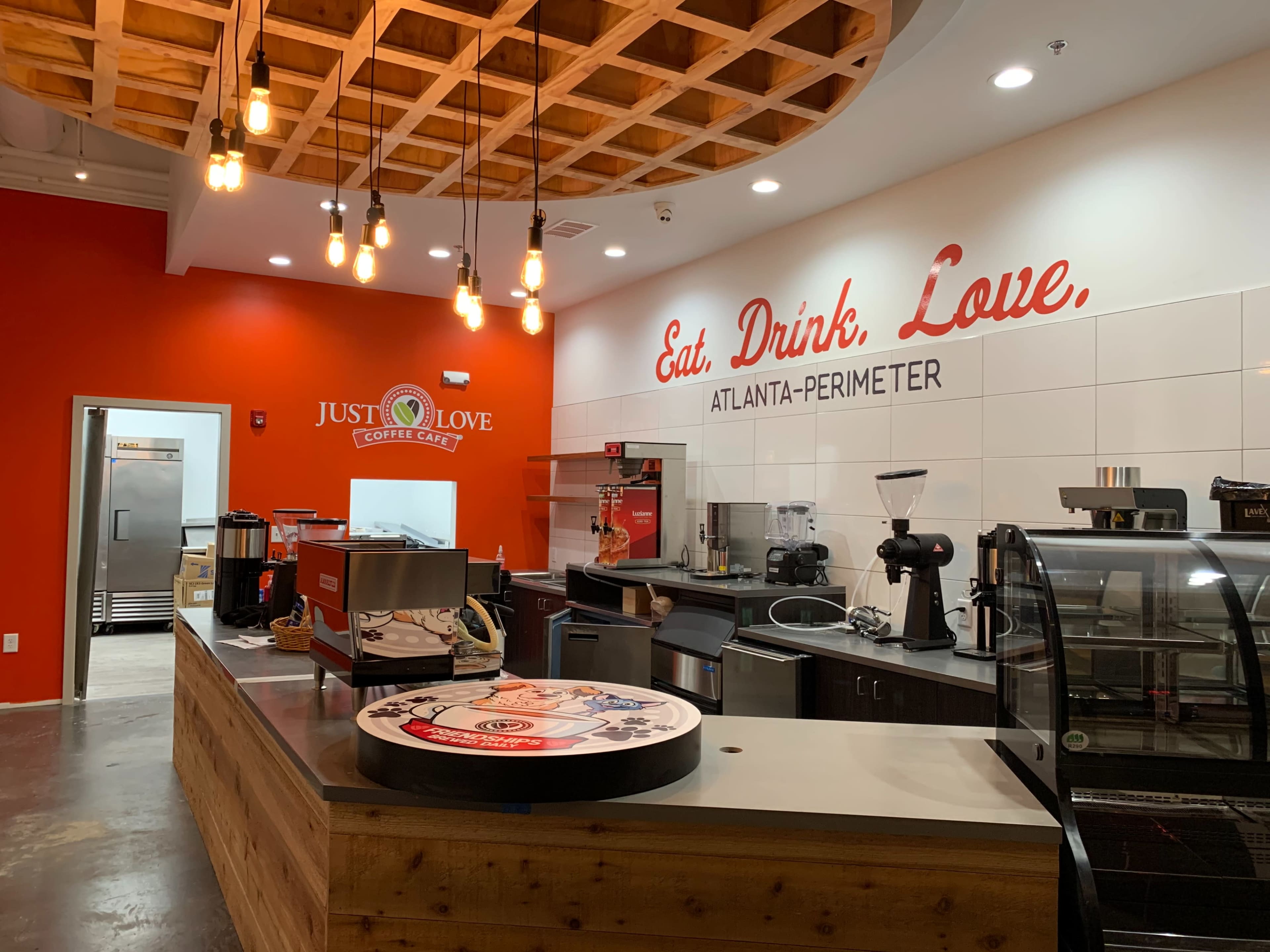 The image shows a coffee shop interior with a welcoming counter, modern appliances, and a bright red accent wall featuring the slogan "Eat, Drink, Love."
