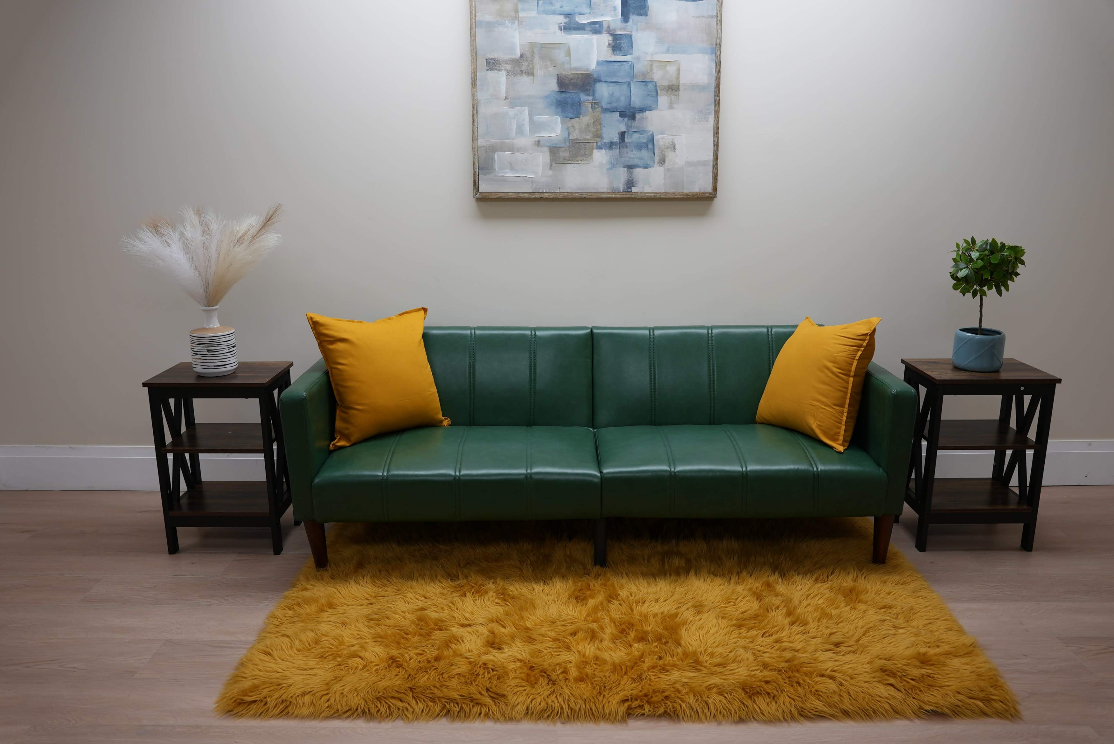 A green couch with yellow pillows is placed on a fluffy yellow rug between two black side tables, with a decorative plant and a vase.