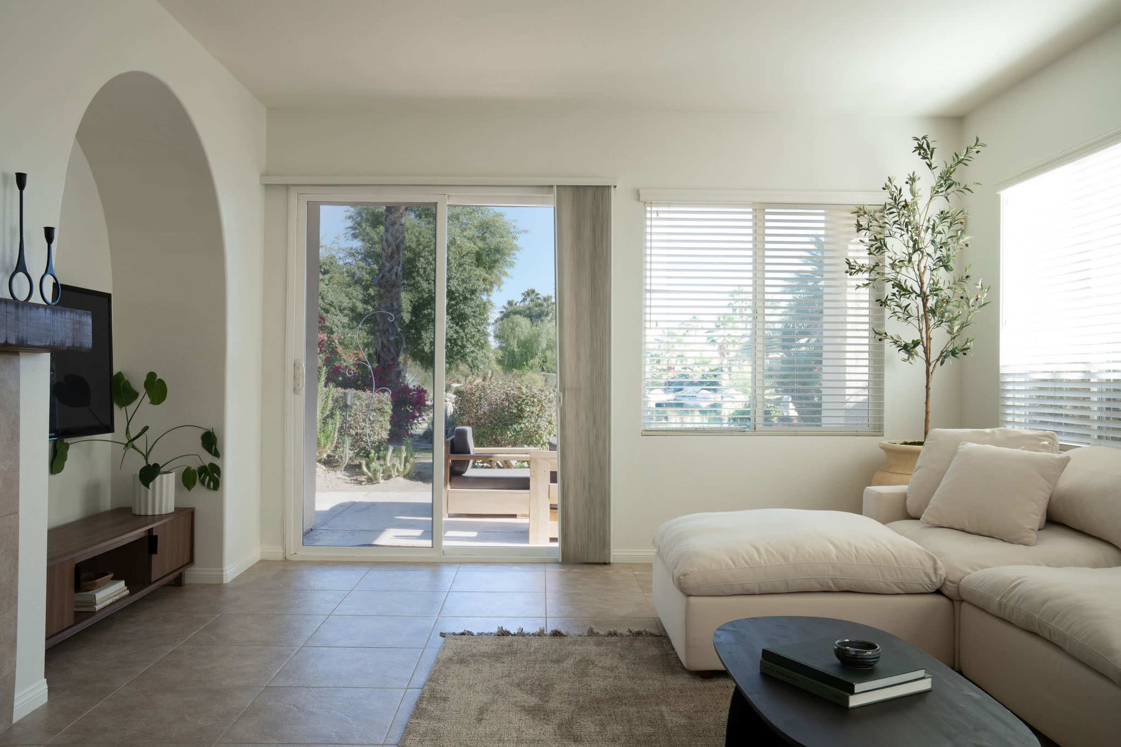 A bright living room with a white sectional sofa, a black coffee table, and large sliding glass doors leading to an outdoor patio.