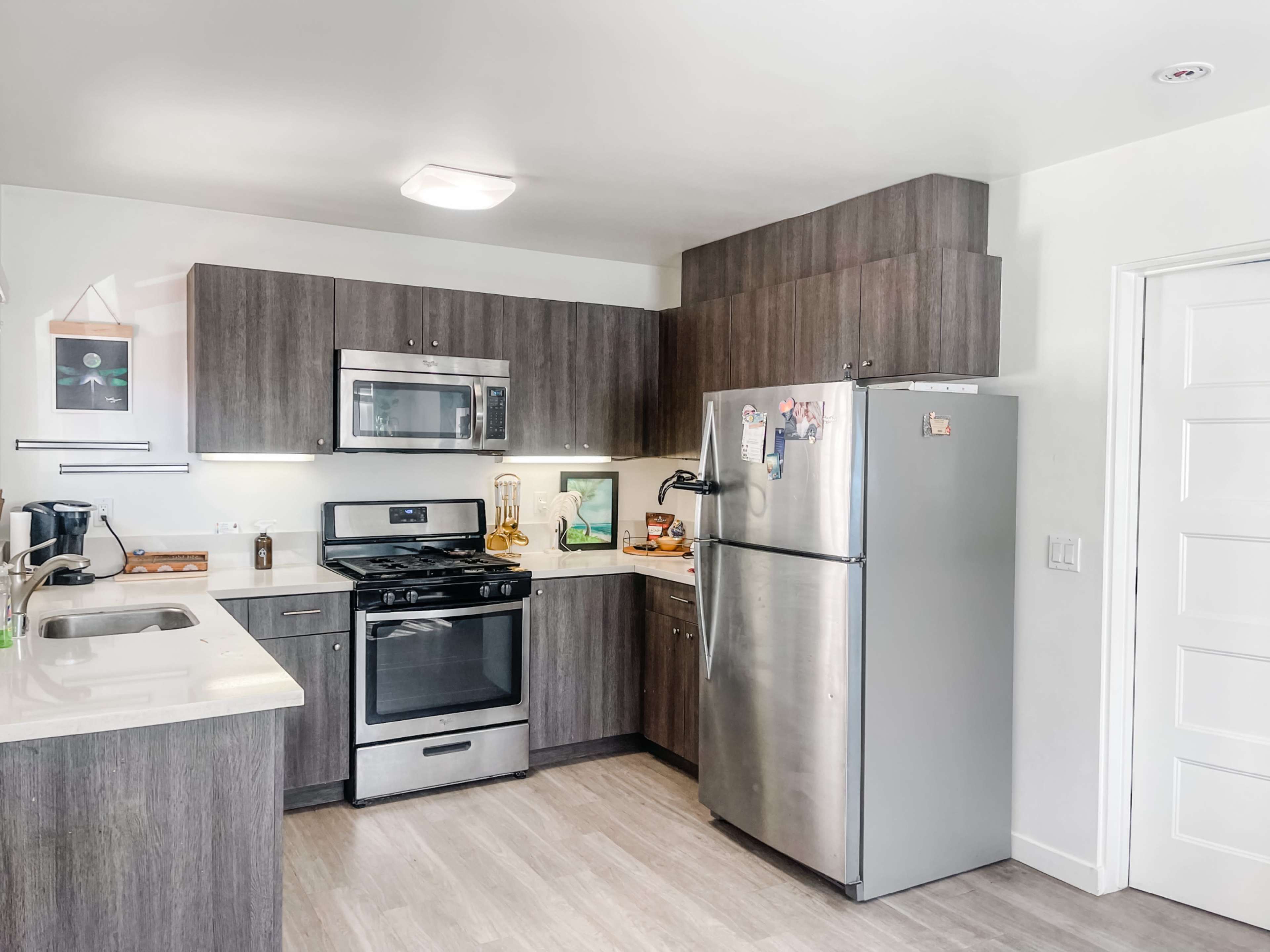 A modern kitchen with stainless steel appliances, dark wood cabinetry, and a light-colored countertop.