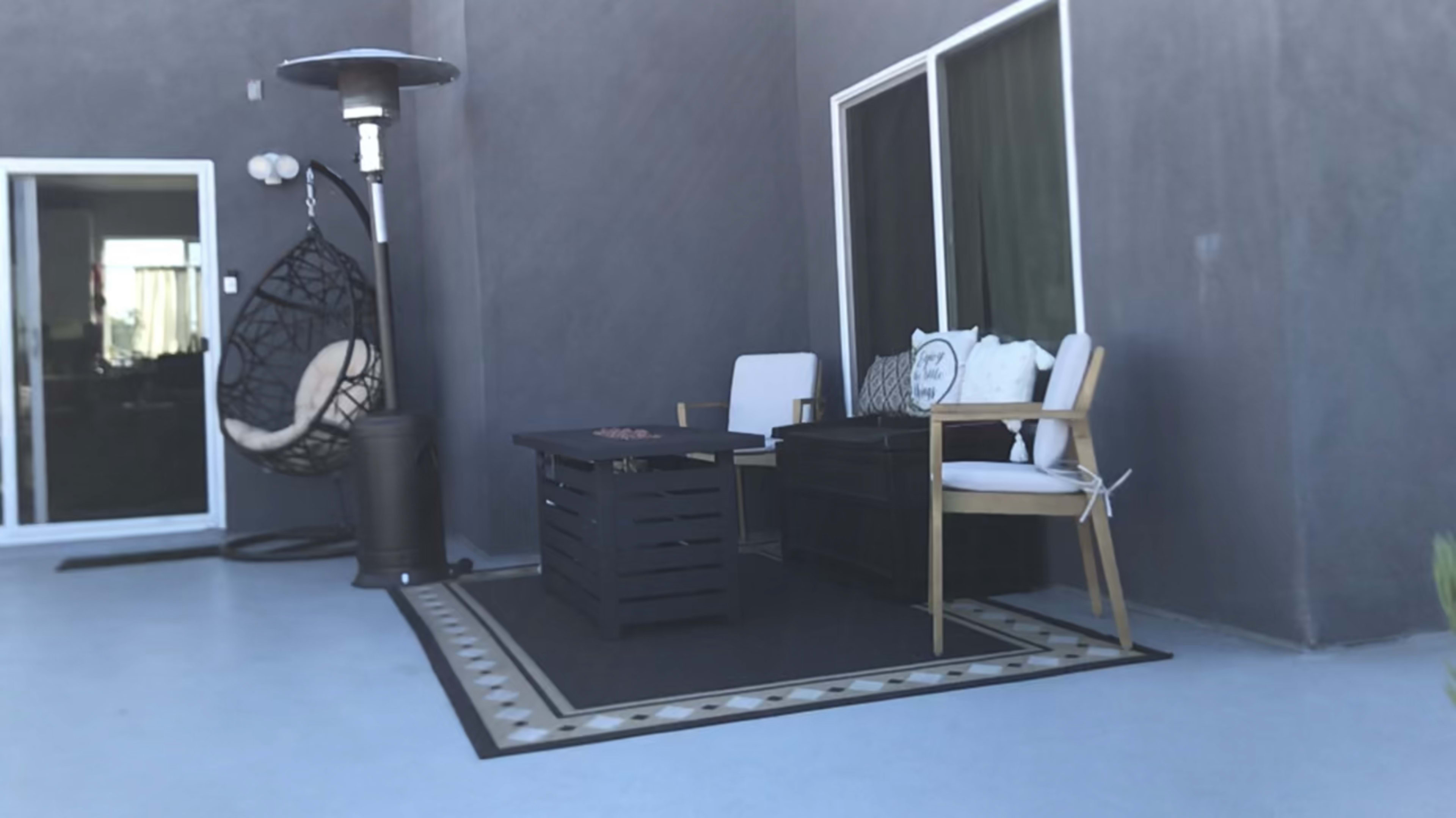 A patio area features a hanging chair, two chairs, a table, and a patterned rug against a gray wall.